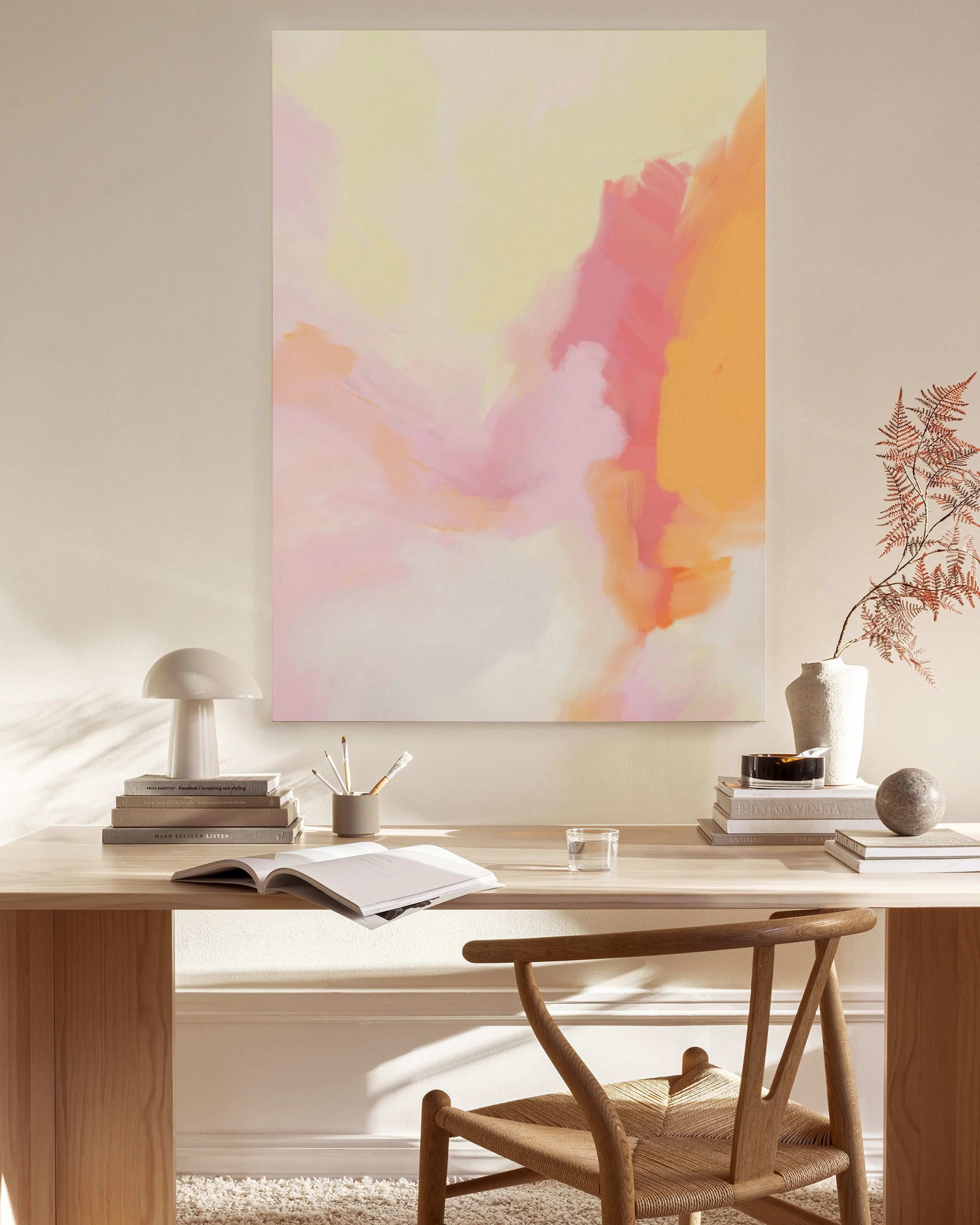 Canvas met abstracte roze, oranje en gele vegen, hangend in een rustige woonkamer boven een dressoir.