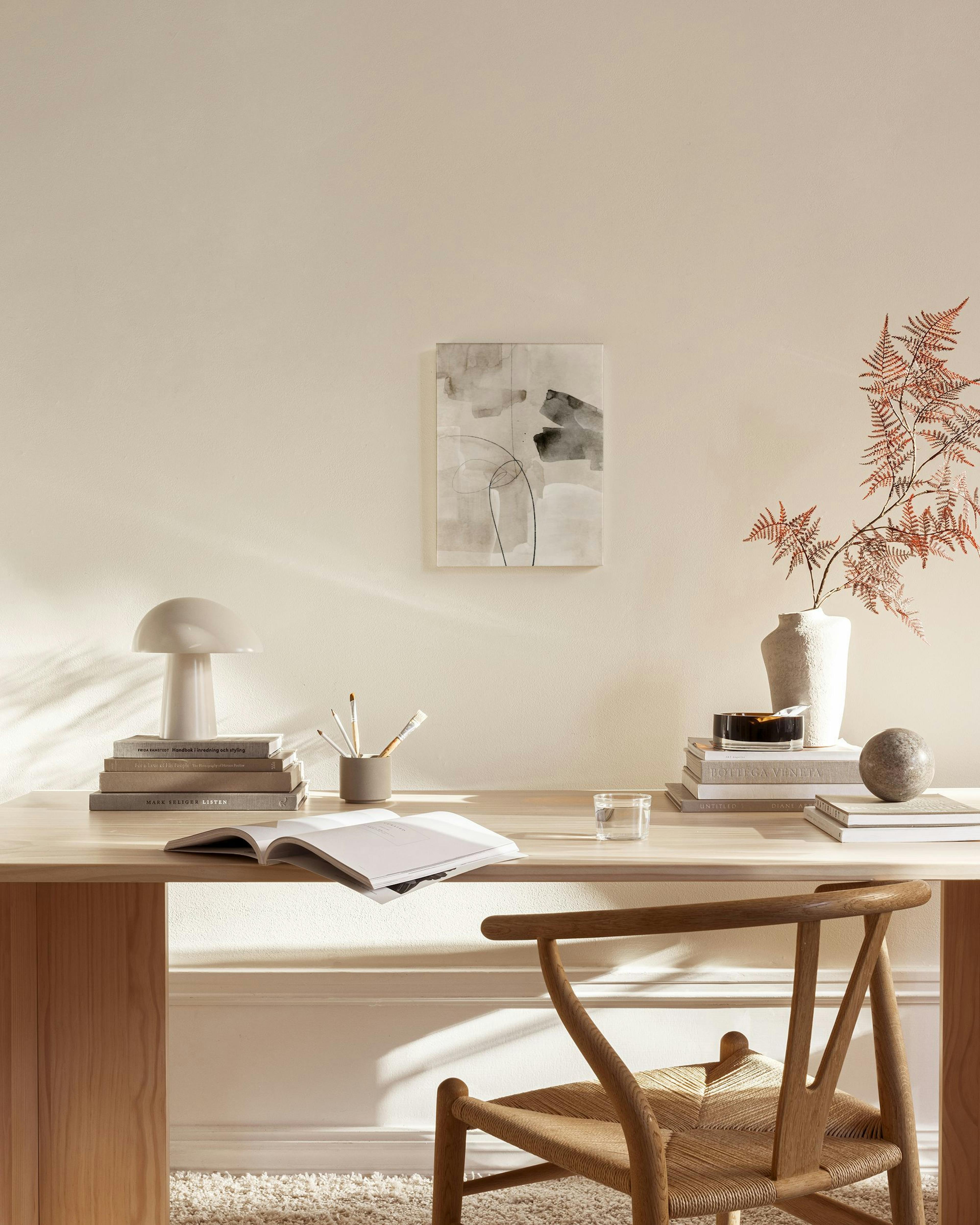 Leinwandbild mit abstrakten Formen in Beige und Grau, schwarzen Linien, in einem hellen Wohnzimmer über einer Holzbank.