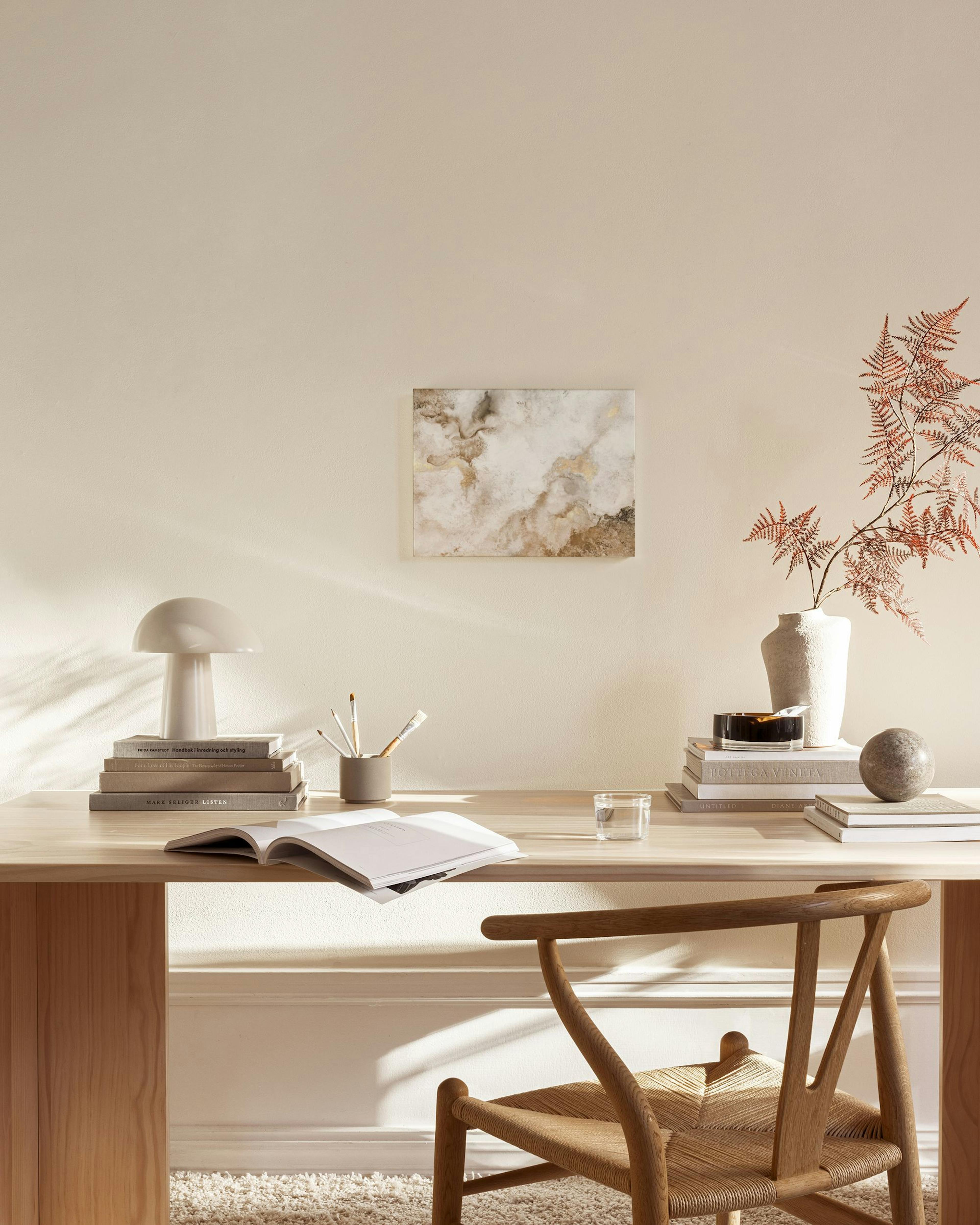 Canvastavla med abstrakta former i guld, beige och brunt, hängande i ett ljust vardagsrum ovanför en bänk.