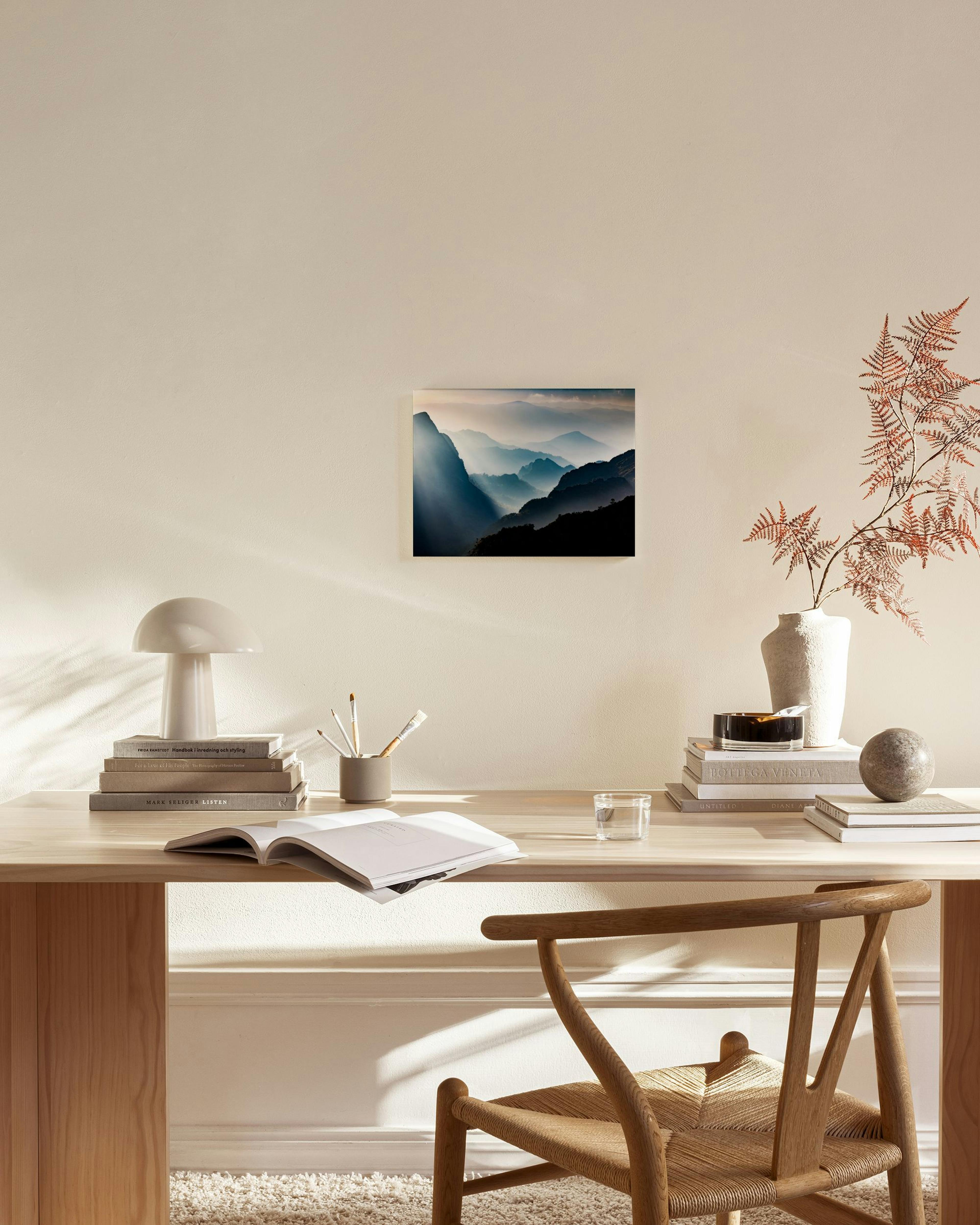 Canvas print of misty blue mountain ranges with sunbeams breaking through, displayed in a minimal living room.