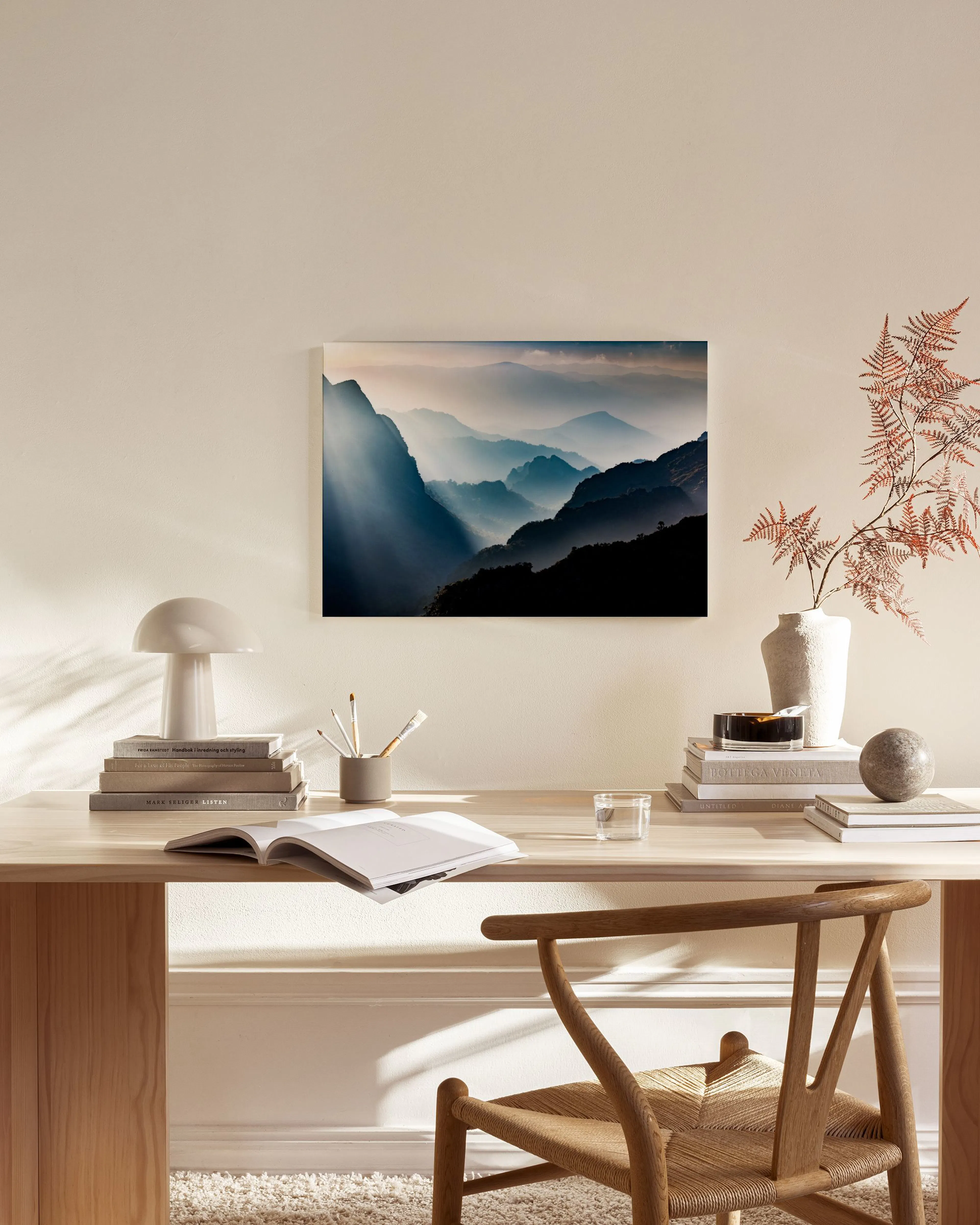 Canvas van berglandschap met mistige valleien en zonnestralen, hangend boven een houten dressoir in een woonkamer.