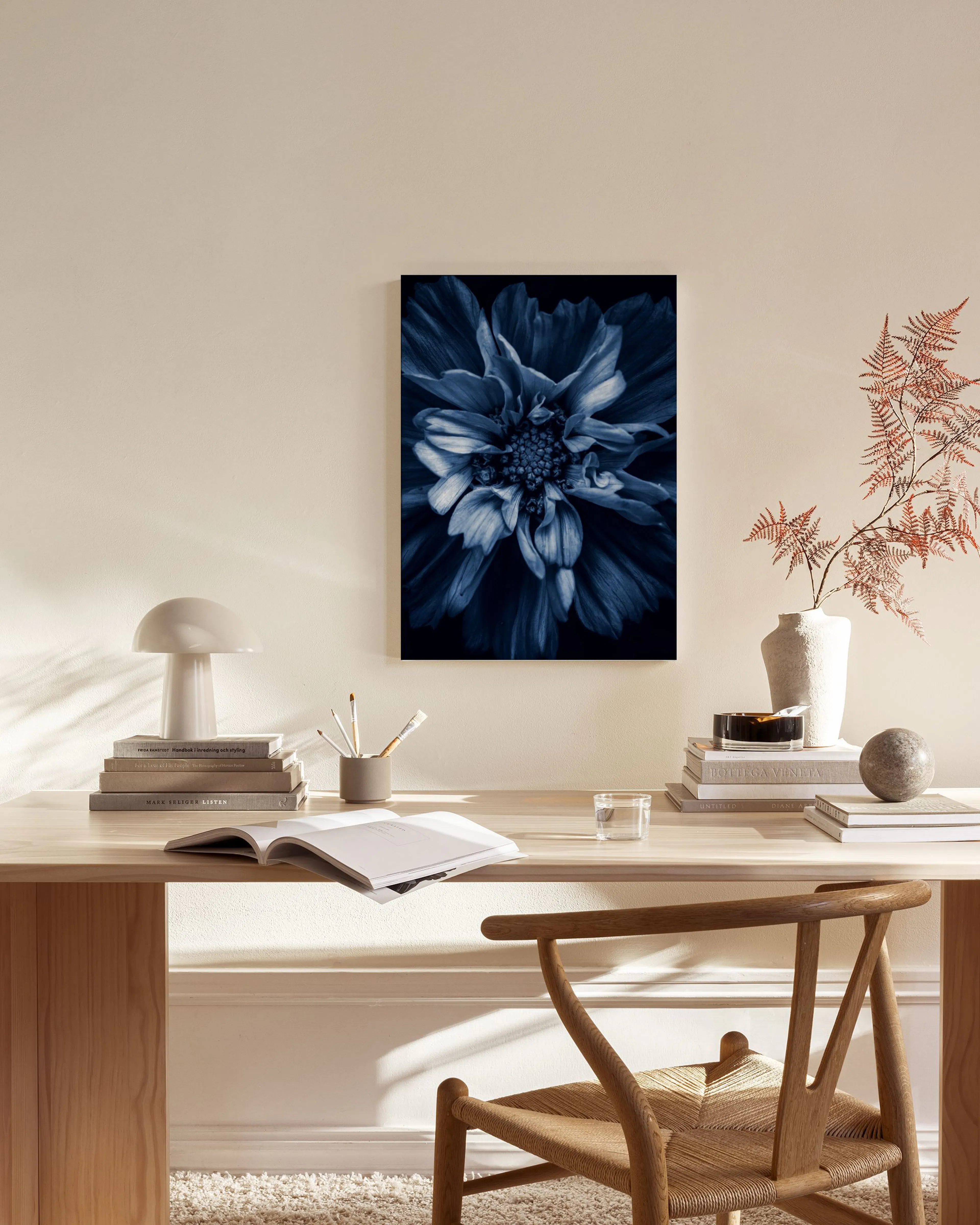 Lienzo de una flor azul oscuro con detalles claros, colgado en una pared beige sobre un mueble de madera en un salón moderno.