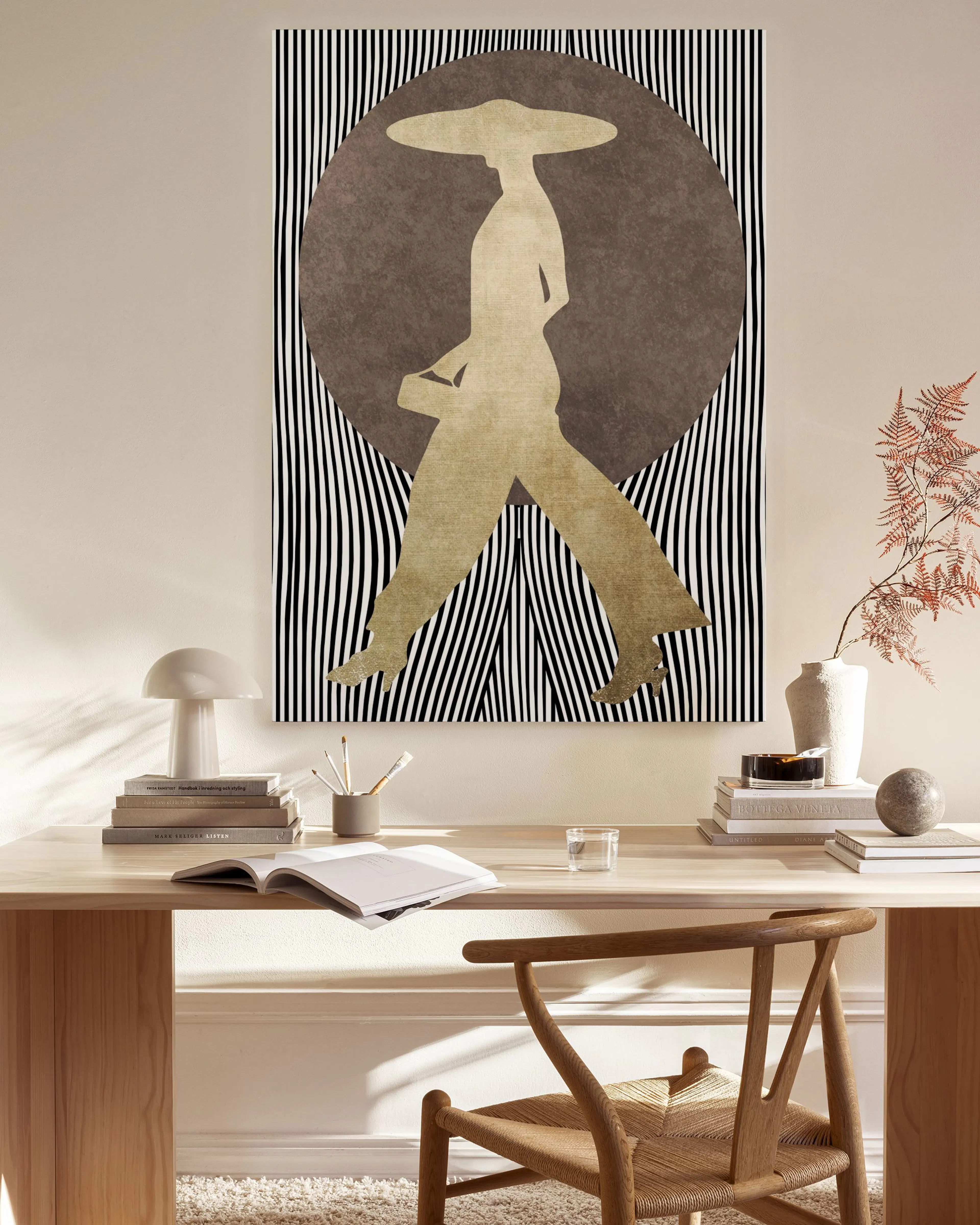 Tela decorativa com figura dourada de mulher de chapéu sobre fundo riscado a preto e branco, pendurada numa sala com mobiliário 
