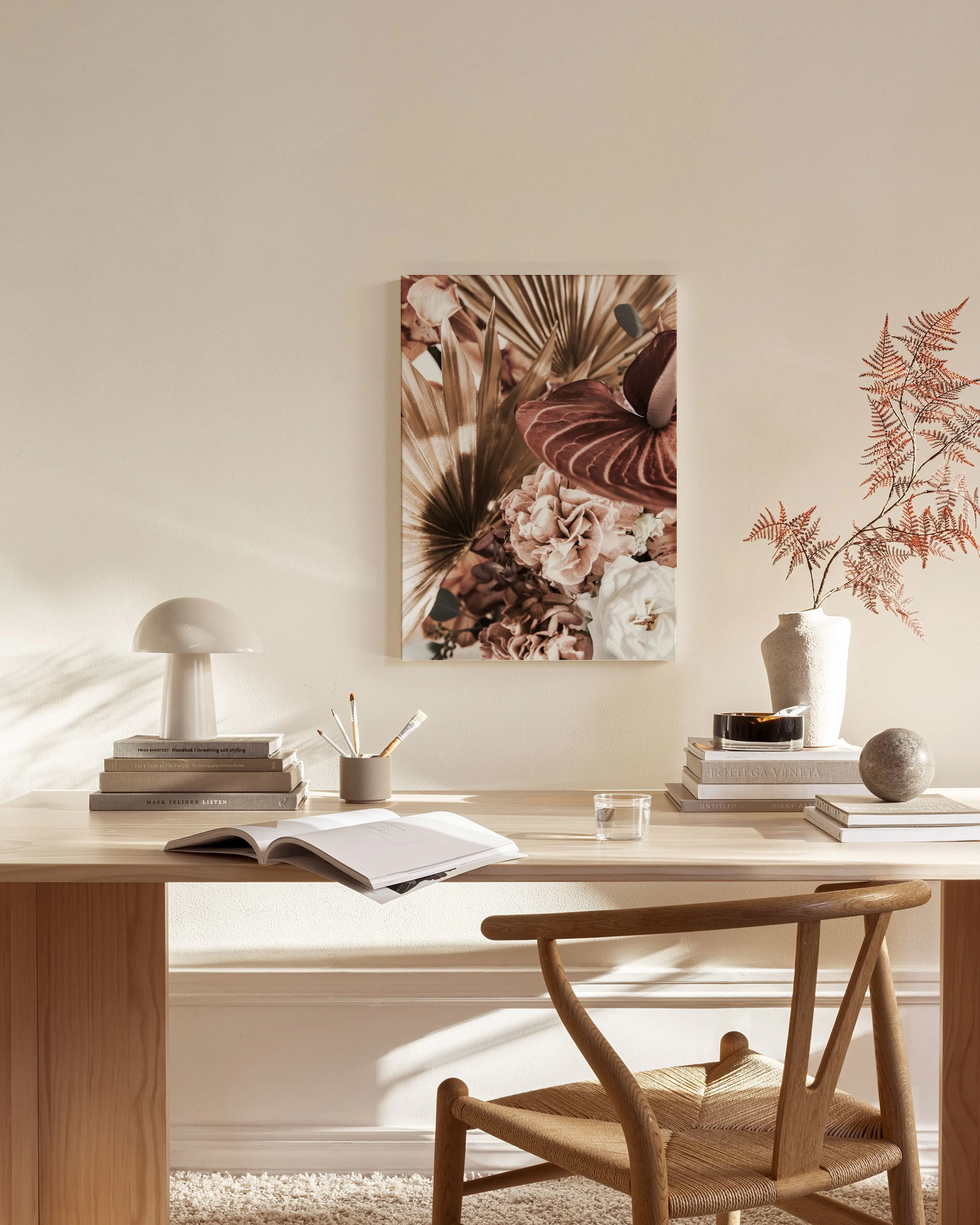 A floral canvas print featuring a bouquet of white and brown flowers with palm leaves, hanging in a minimalist living room.
