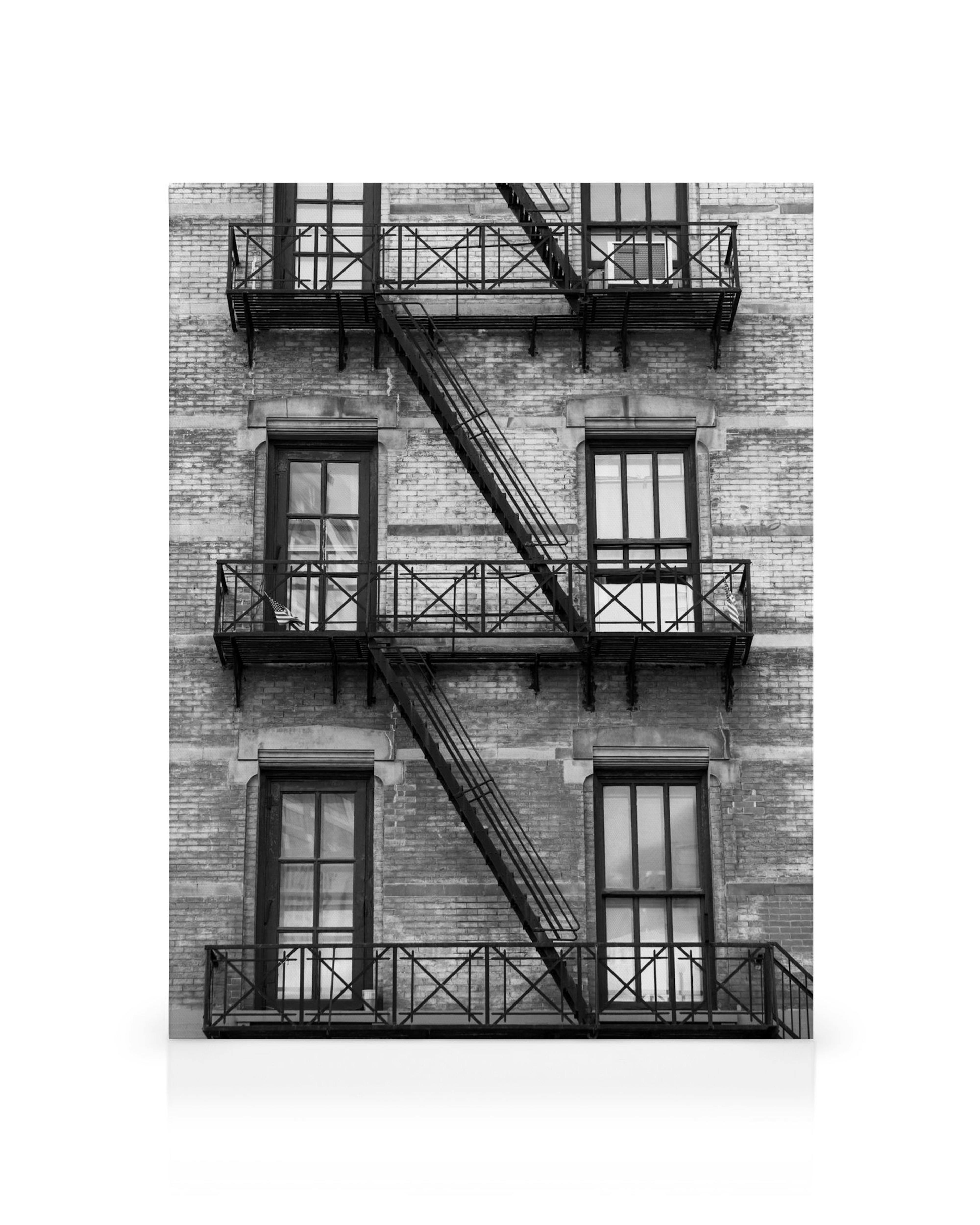 Fachada de ladrillo blanco y negro con escaleras de incendios en zigzag, arte industrial urbano.