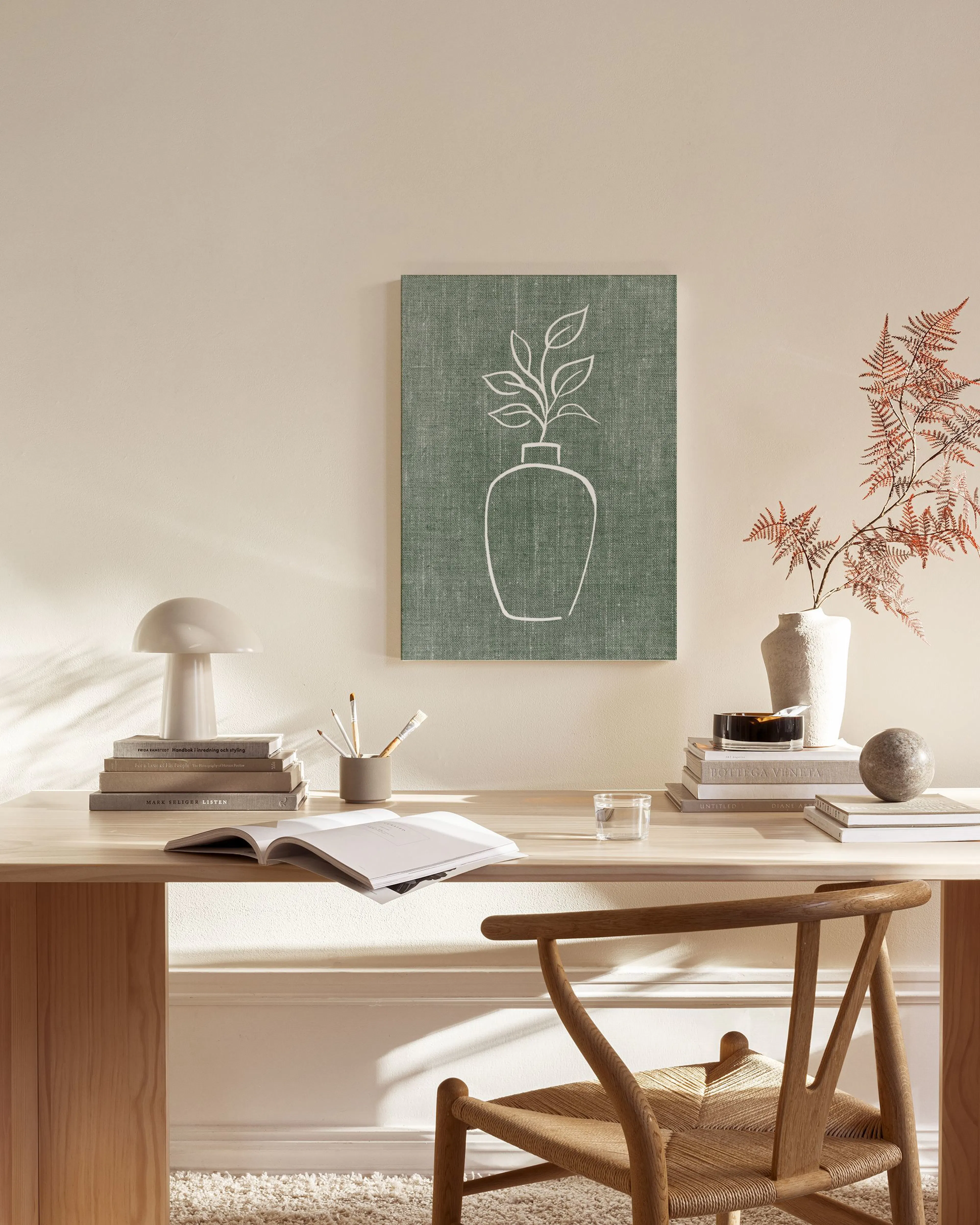 Lærred med en hvid lineart tegning af en plante i en vase på grøn baggrund, hængende i en stue.