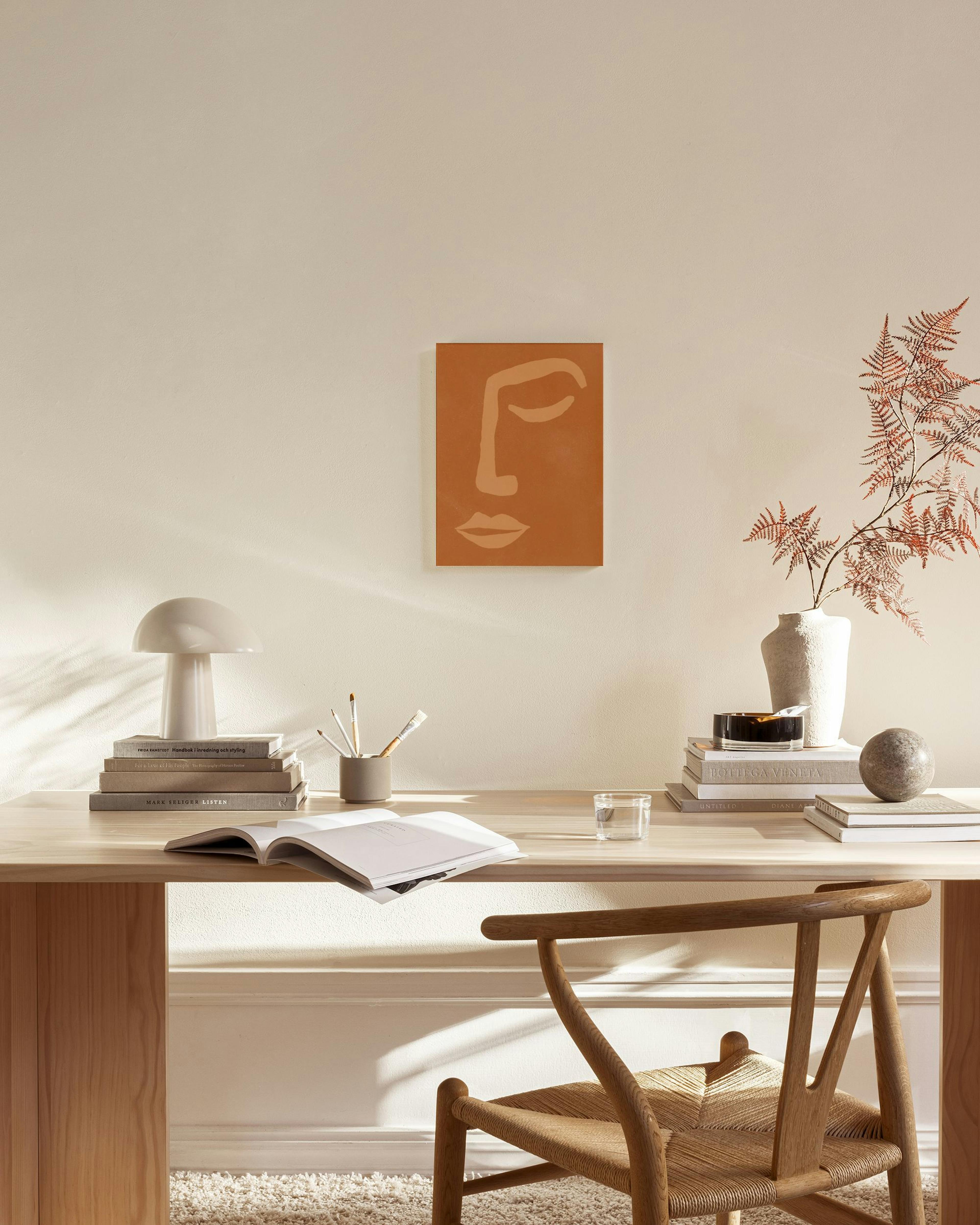 A canvas print of an abstract face in terracotta and beige, hanging in a minimalist living room above a wooden console.