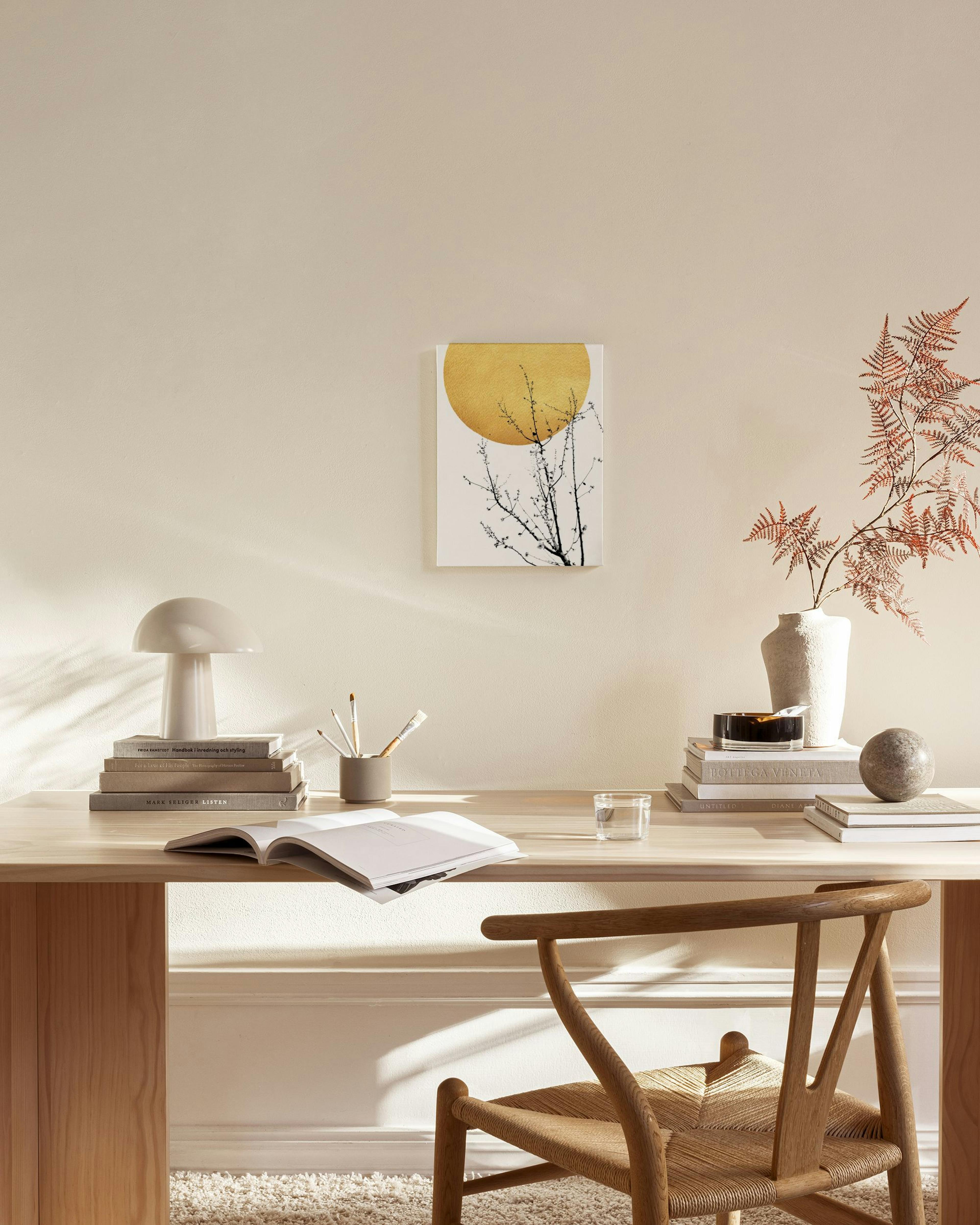 Stampa su tela con un albero dai rami intricati davanti a un sole dorato, appesa in un salotto moderno.