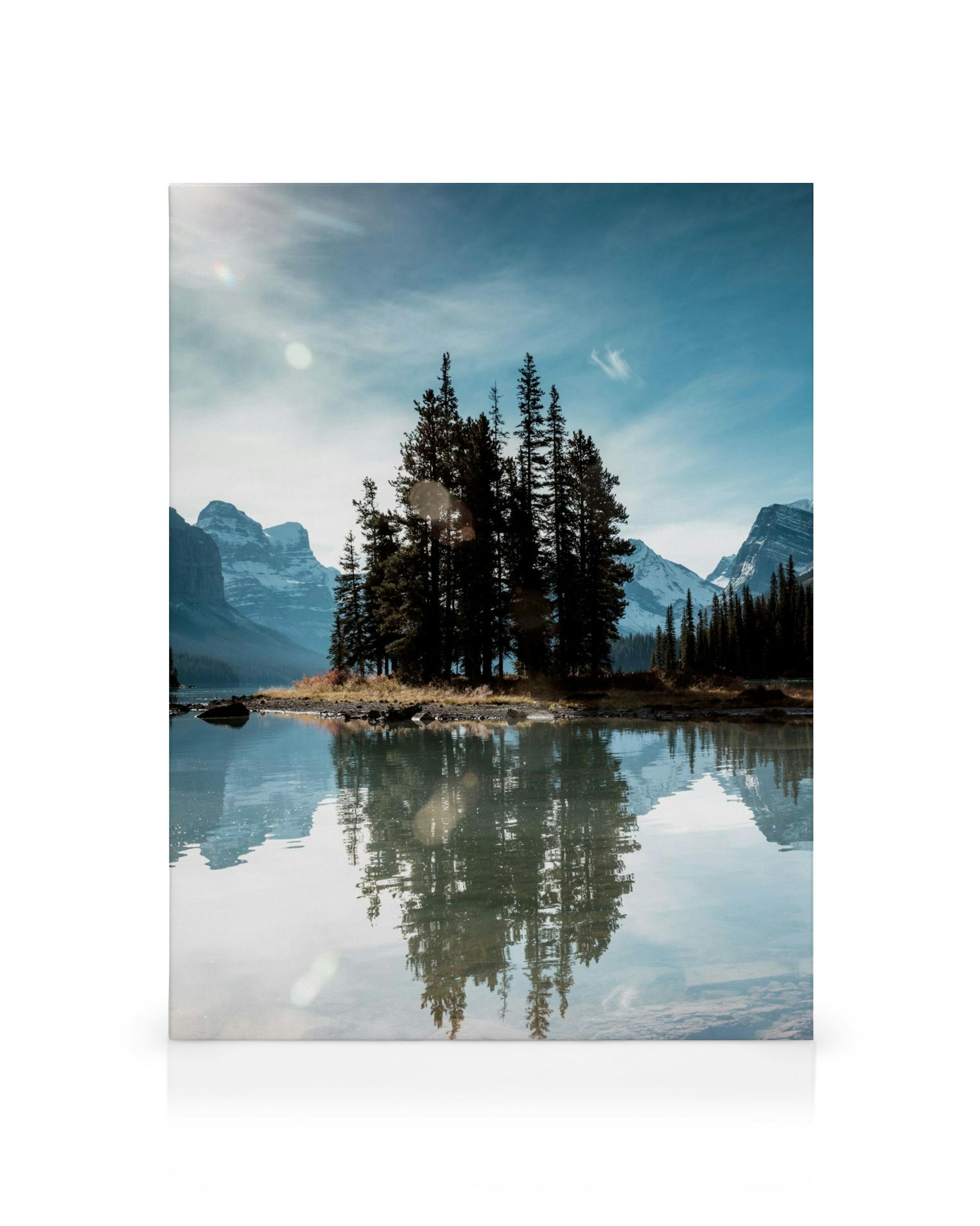 Kanvaasitaulu esittää saarta, jolla on mäntyjä keskellä järveä, lumihuippuisia vuoria taustalla, heijastuen veteen.