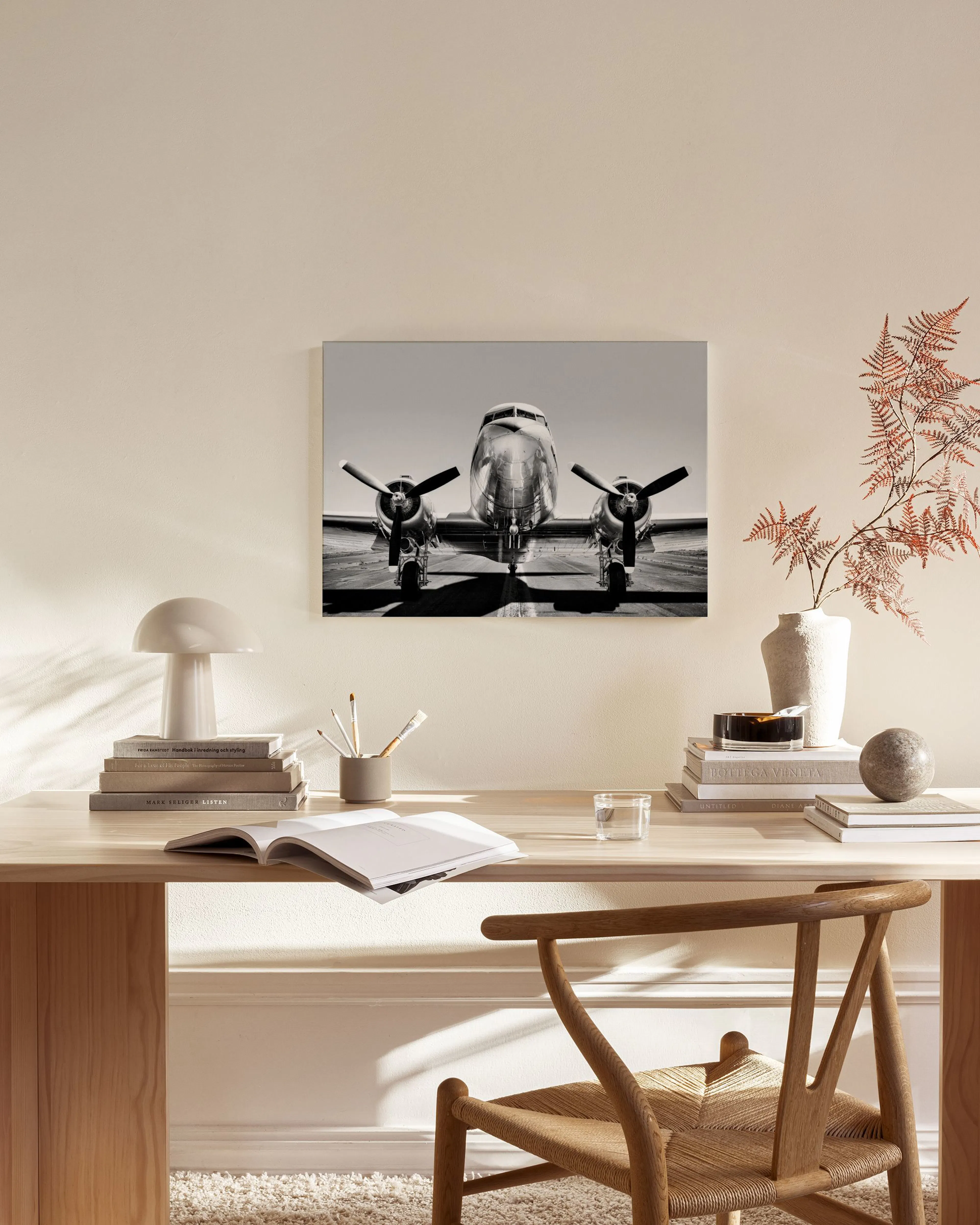 A black and white canvas print of a vintage airplane, head-on view, hanging above a wooden console table in a minimalist living 