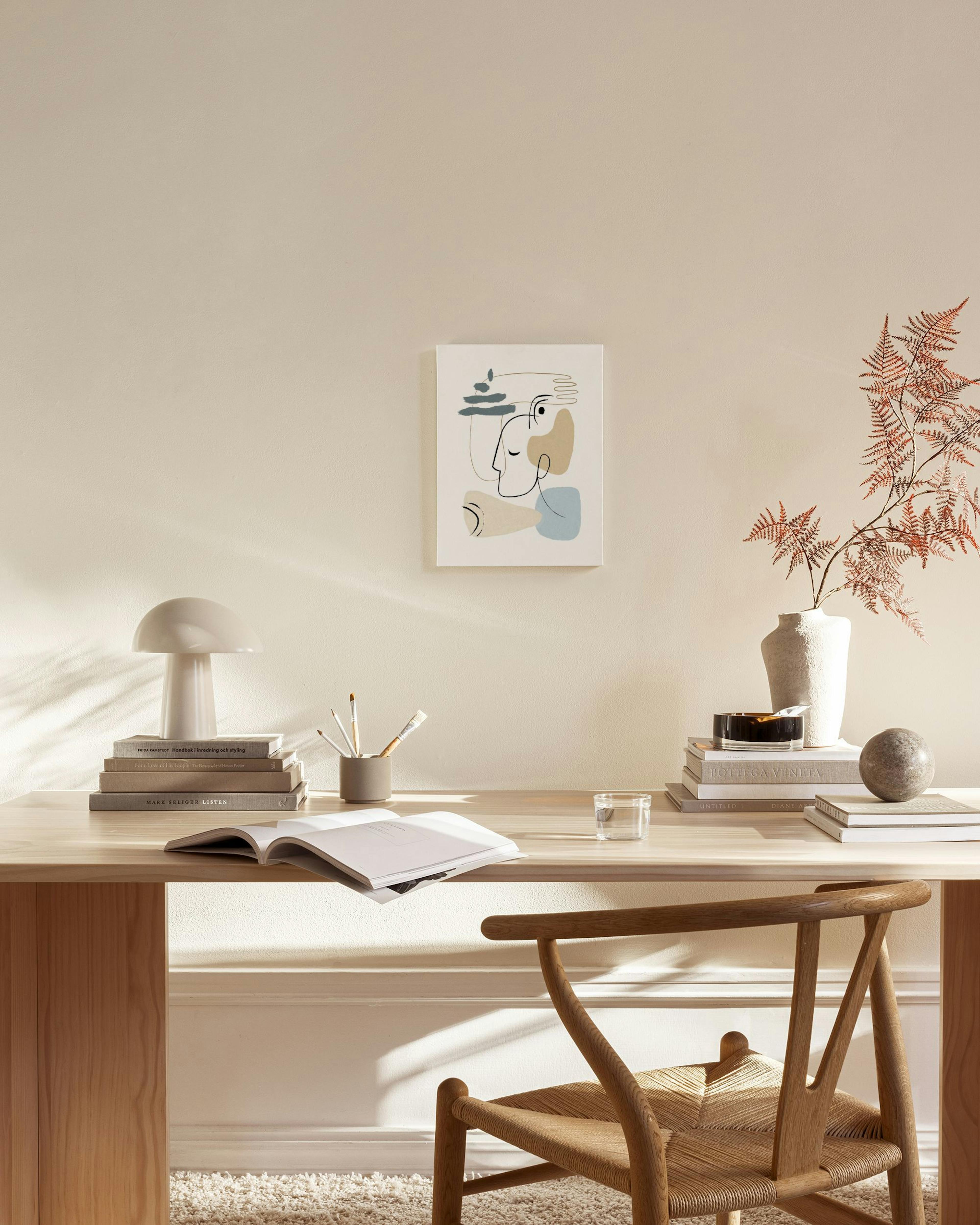 Een canvas met abstracte gezichten in zwarte lijnen, beige en blauwe vormen, hangend in een neutrale woonkamer boven een dressoi