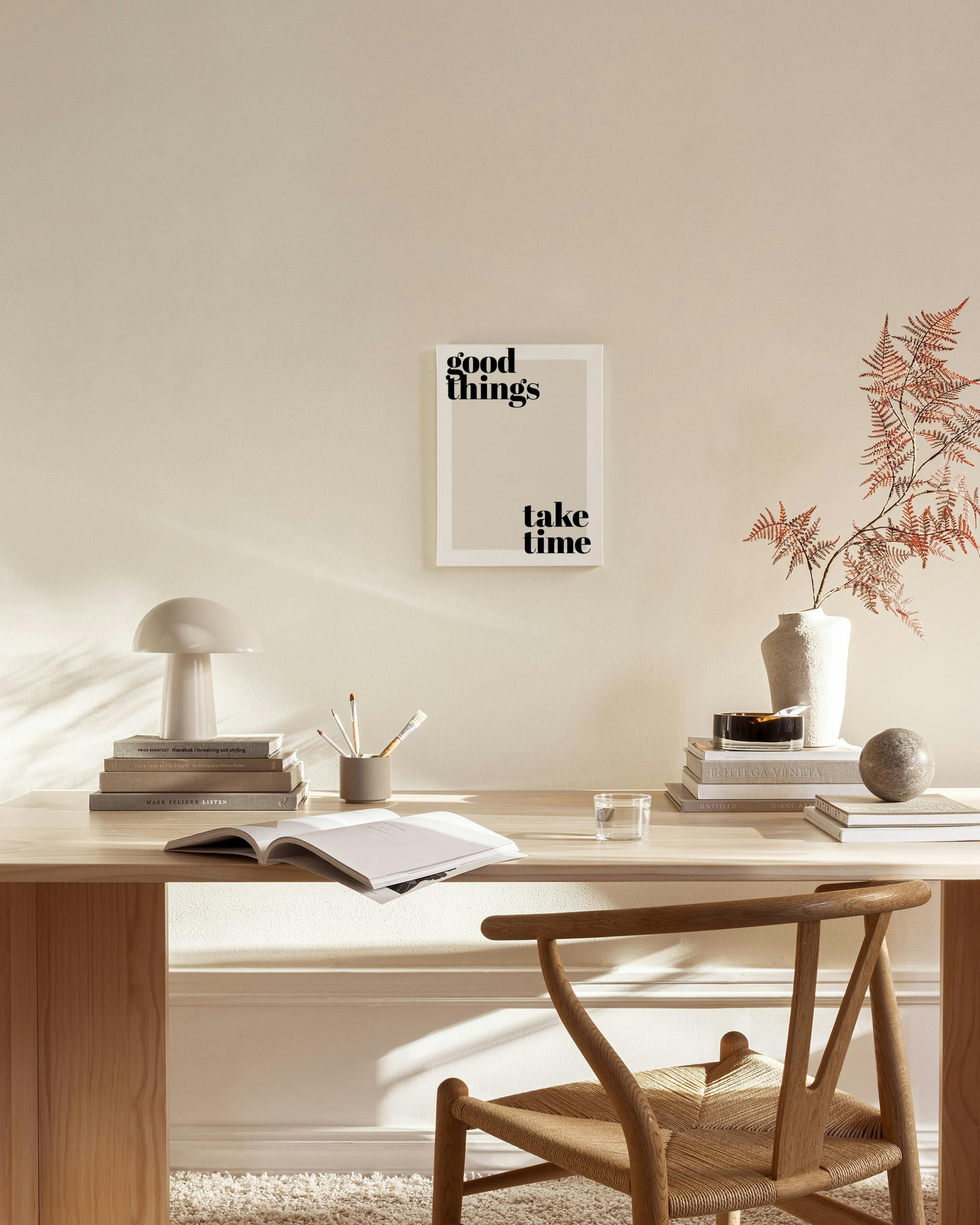 Stampa su tela con la frase good things take time in nero su sfondo beige, appesa sopra una panca in un salotto moderno.