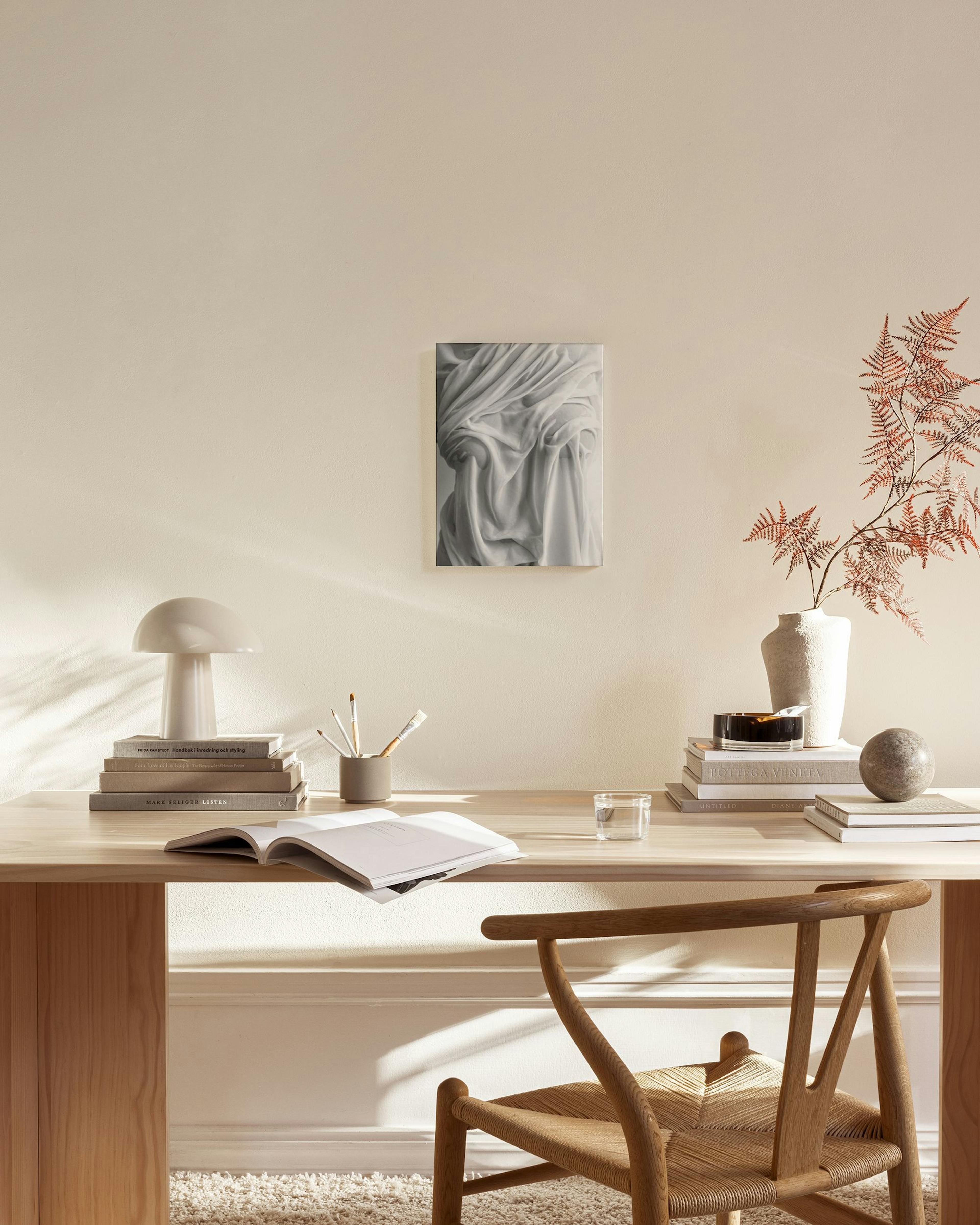 Canvastavla med gråskalebild av draperat tyg, upphängd i ett ljust vardagsrum med soffbord och fåtölj.