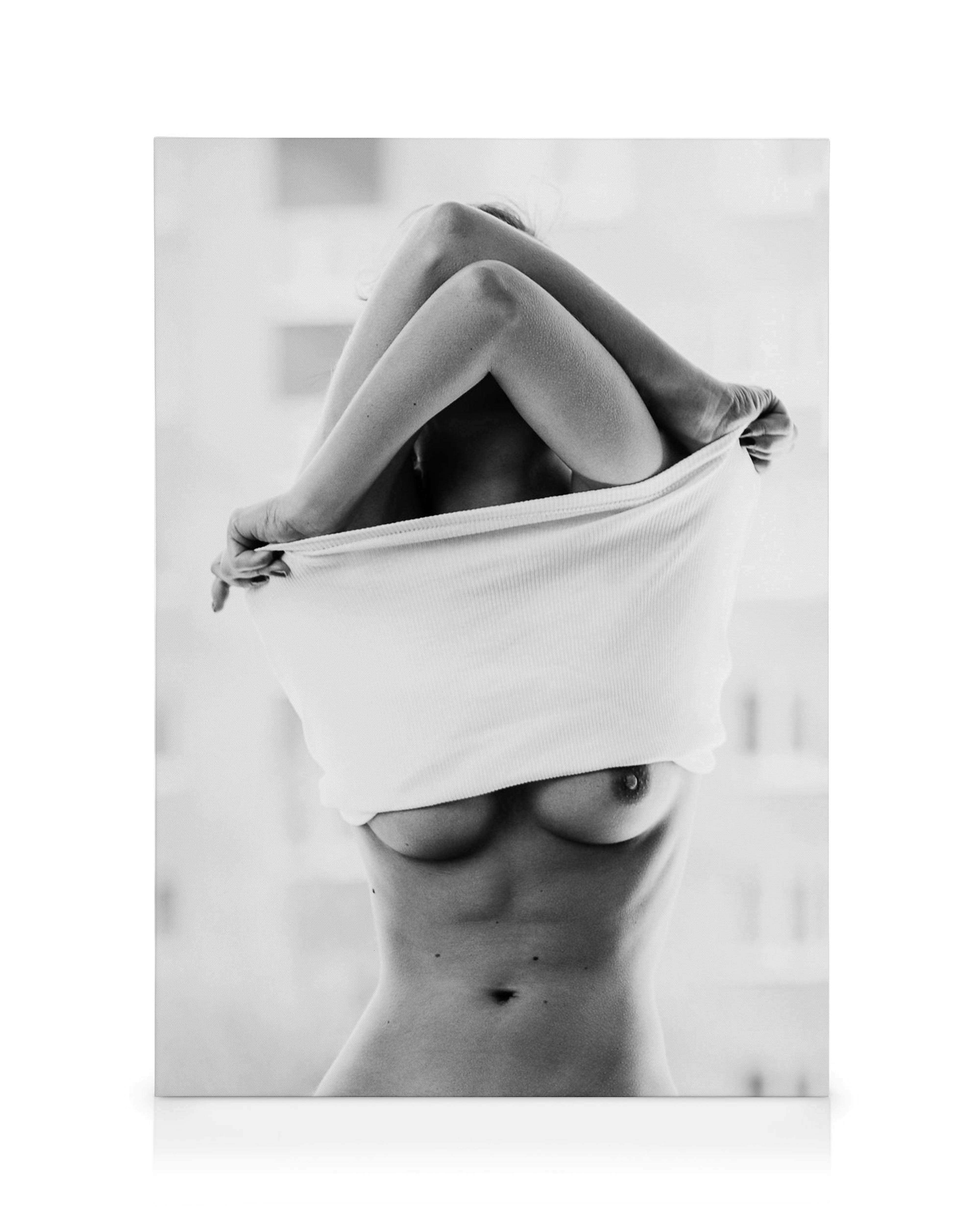 Sorthvidt lærred. Kvinde tager hvid top af, hænder over hovedet, nøgen overkrop, sensuel kunst.