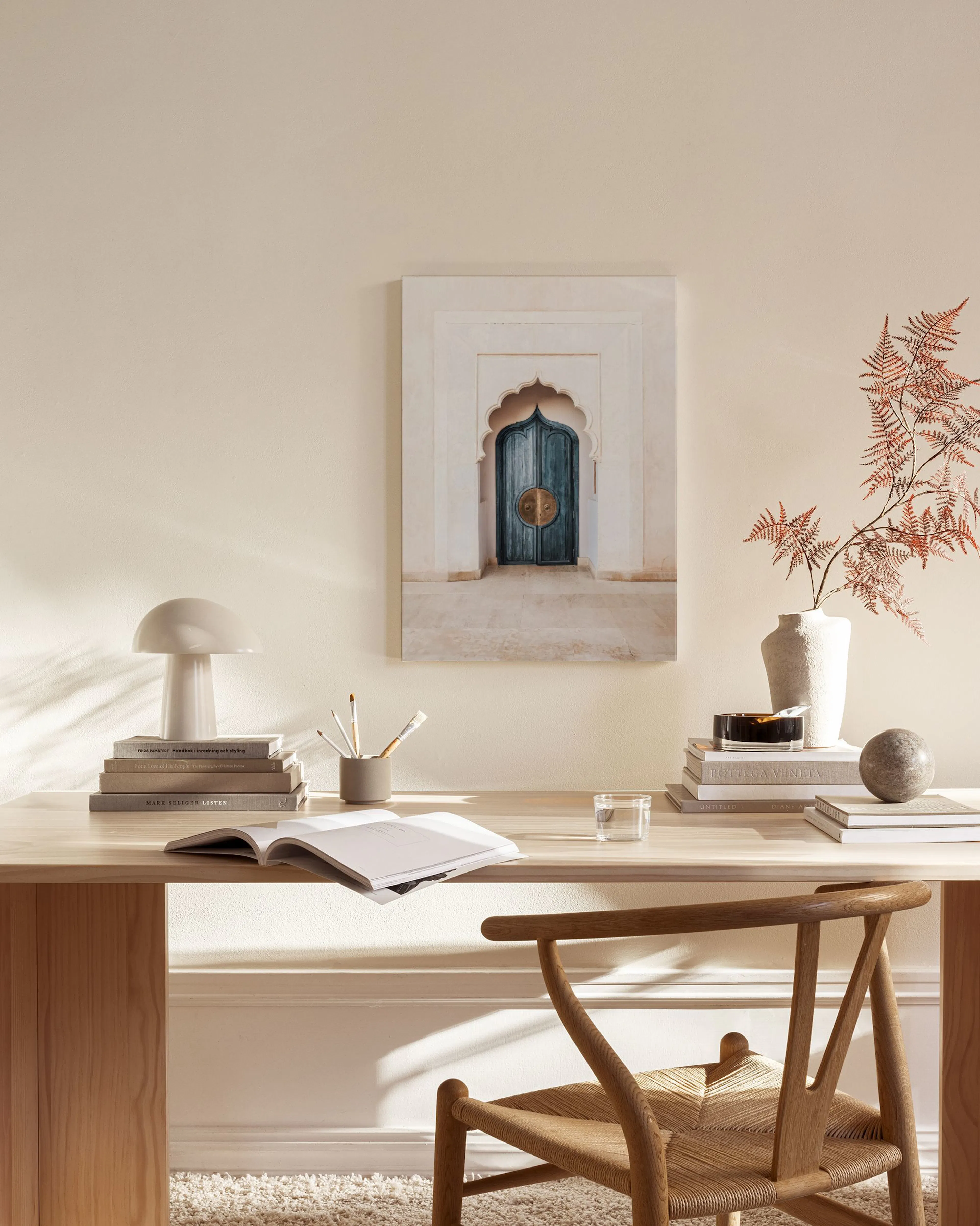 A canvas print of an ornate teal door within a light arched alcove, displayed above a wooden console table in a minimalist livin