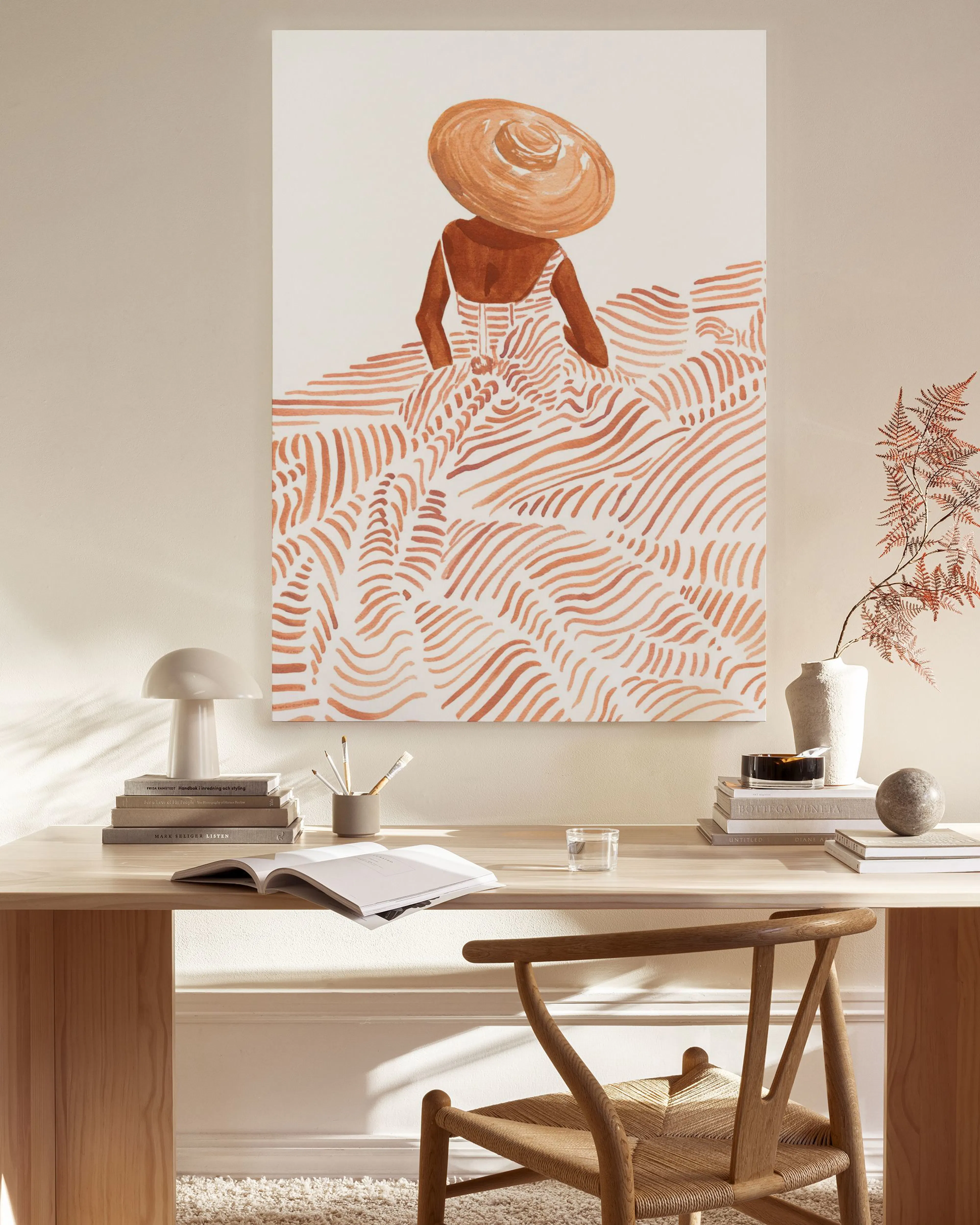 Lærred med illustreret kvinde med stråhat og orange mønstret kjole, hængende over et sidebord i stuen.