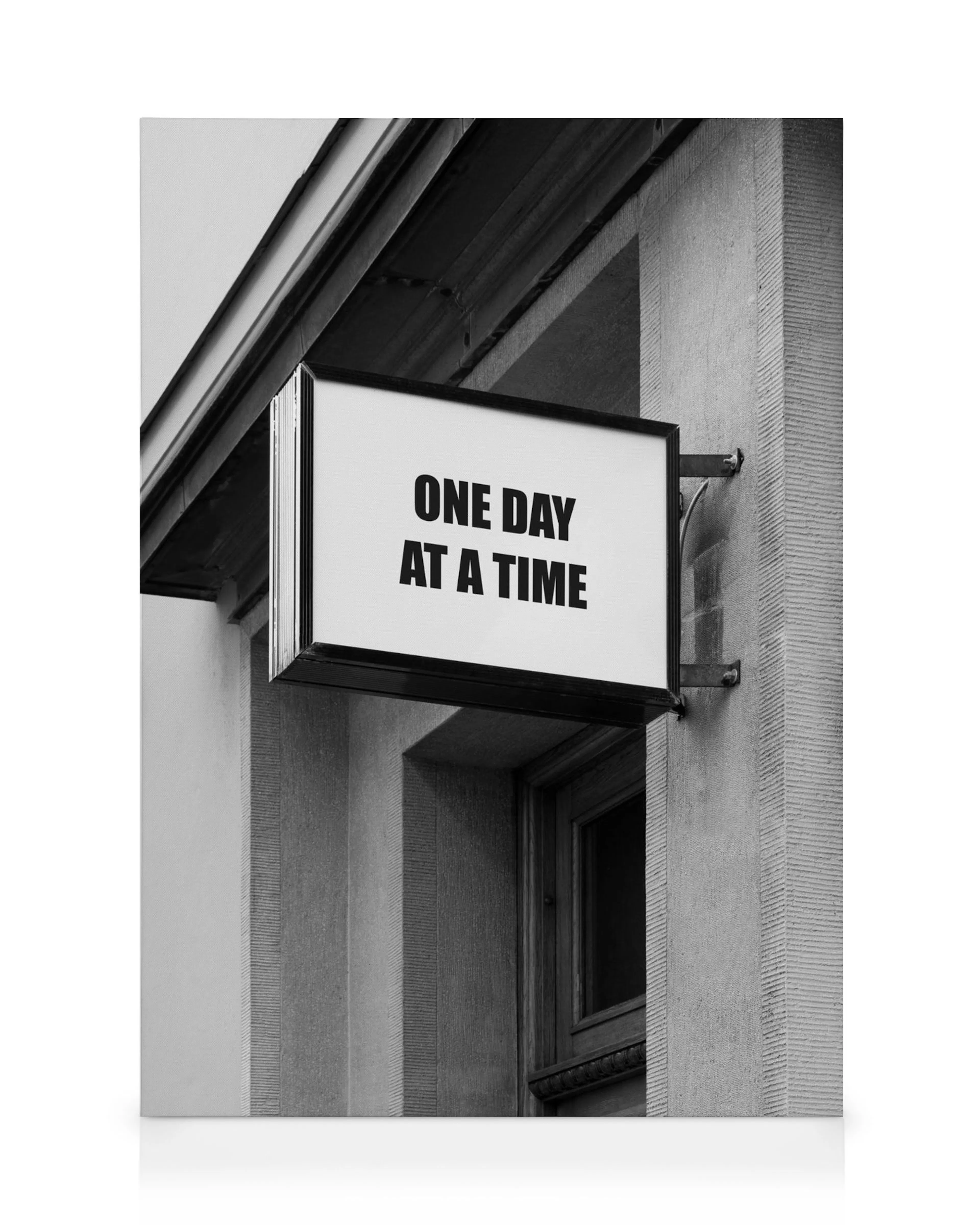 Schwarz-weißes Leinwandbild mit Schild ONE DAY AT A TIME in Großbuchstaben an einer Gebäudewand. Ein Fenster ist unten rechts si