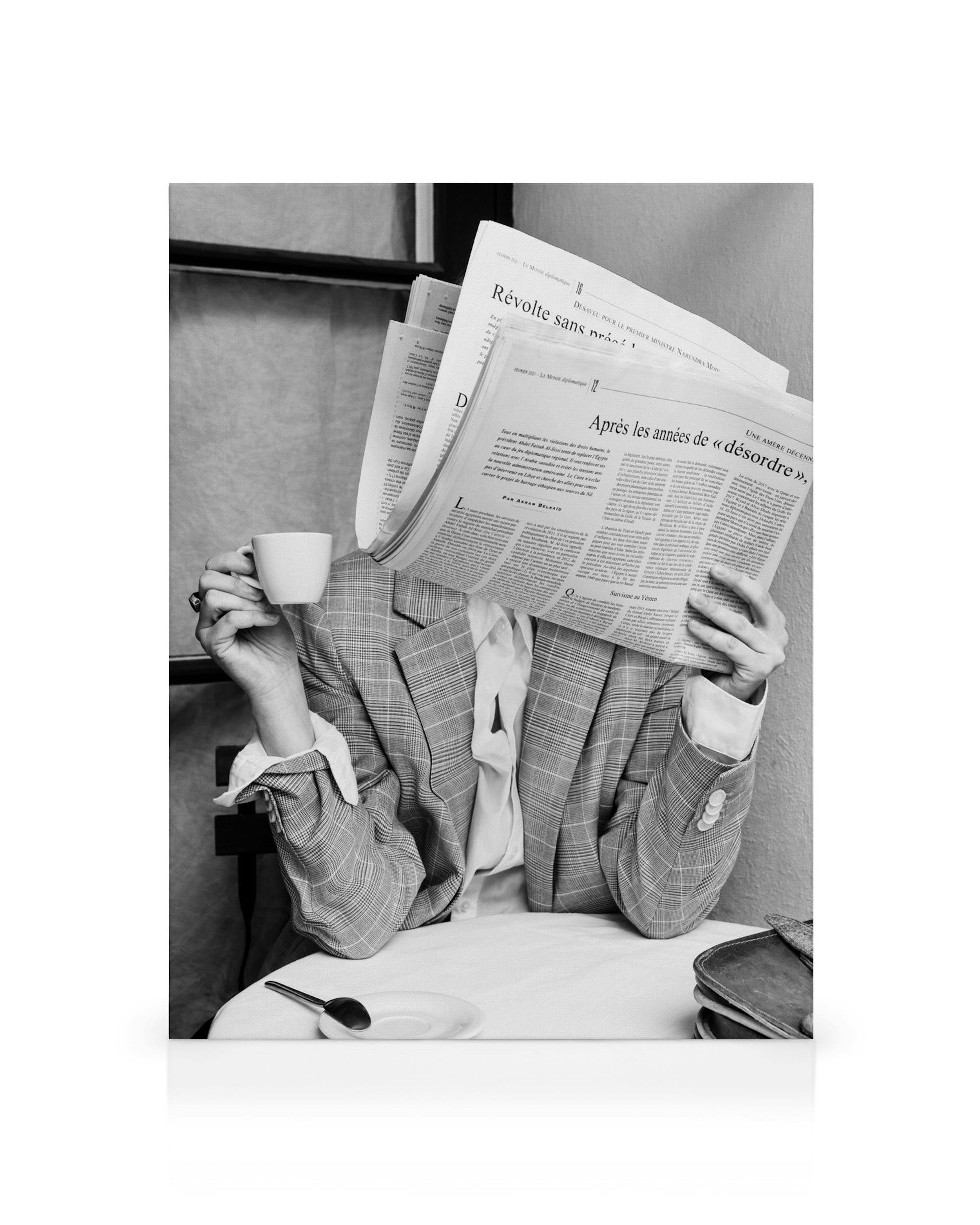 Black and white canvas print of a person reading a newspaper at a cafe table, holding a coffee cup, wearing a checkered jacket.