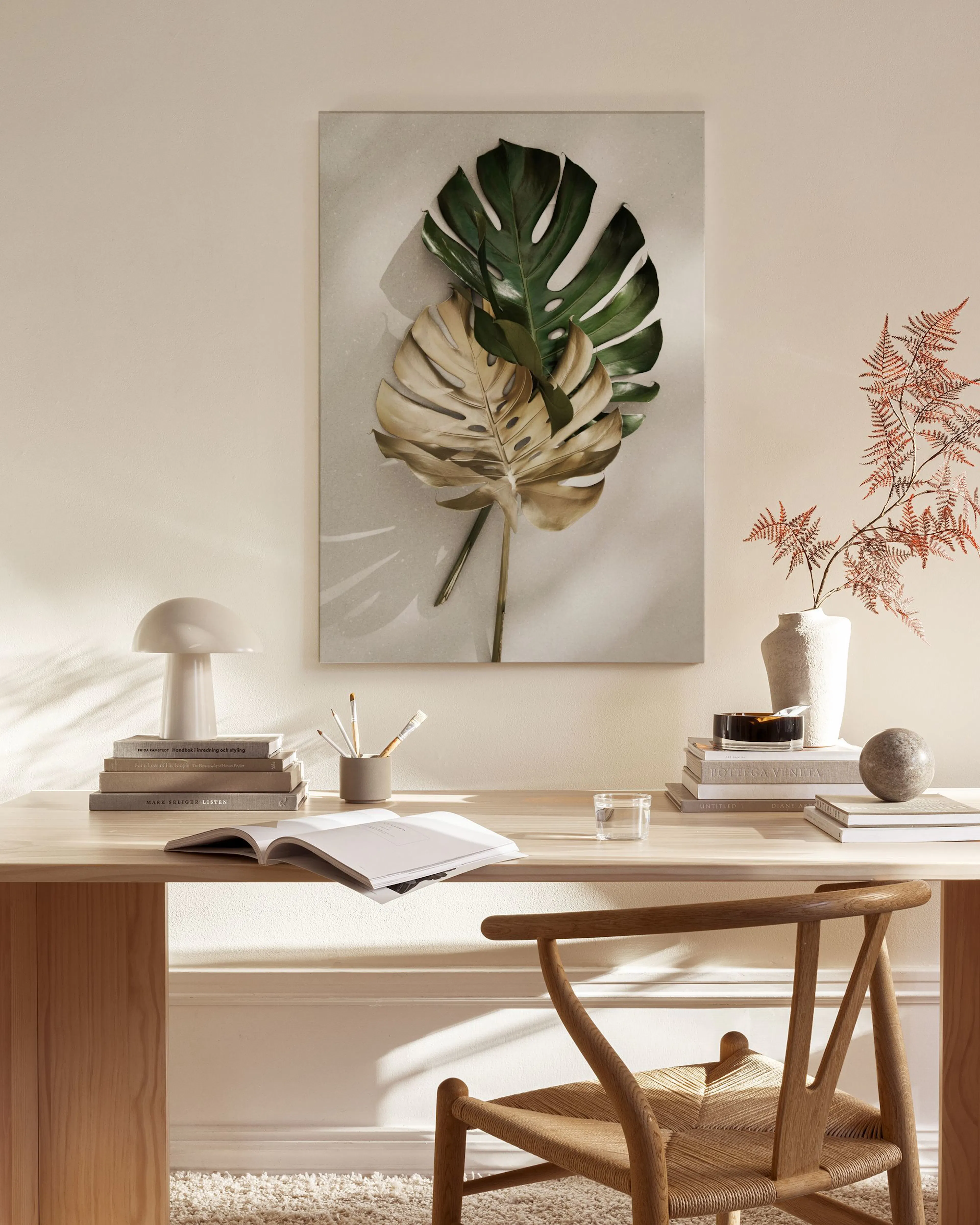 A canvas print of two monstera leaves, one green and one gold, hanging in a minimalist living room.