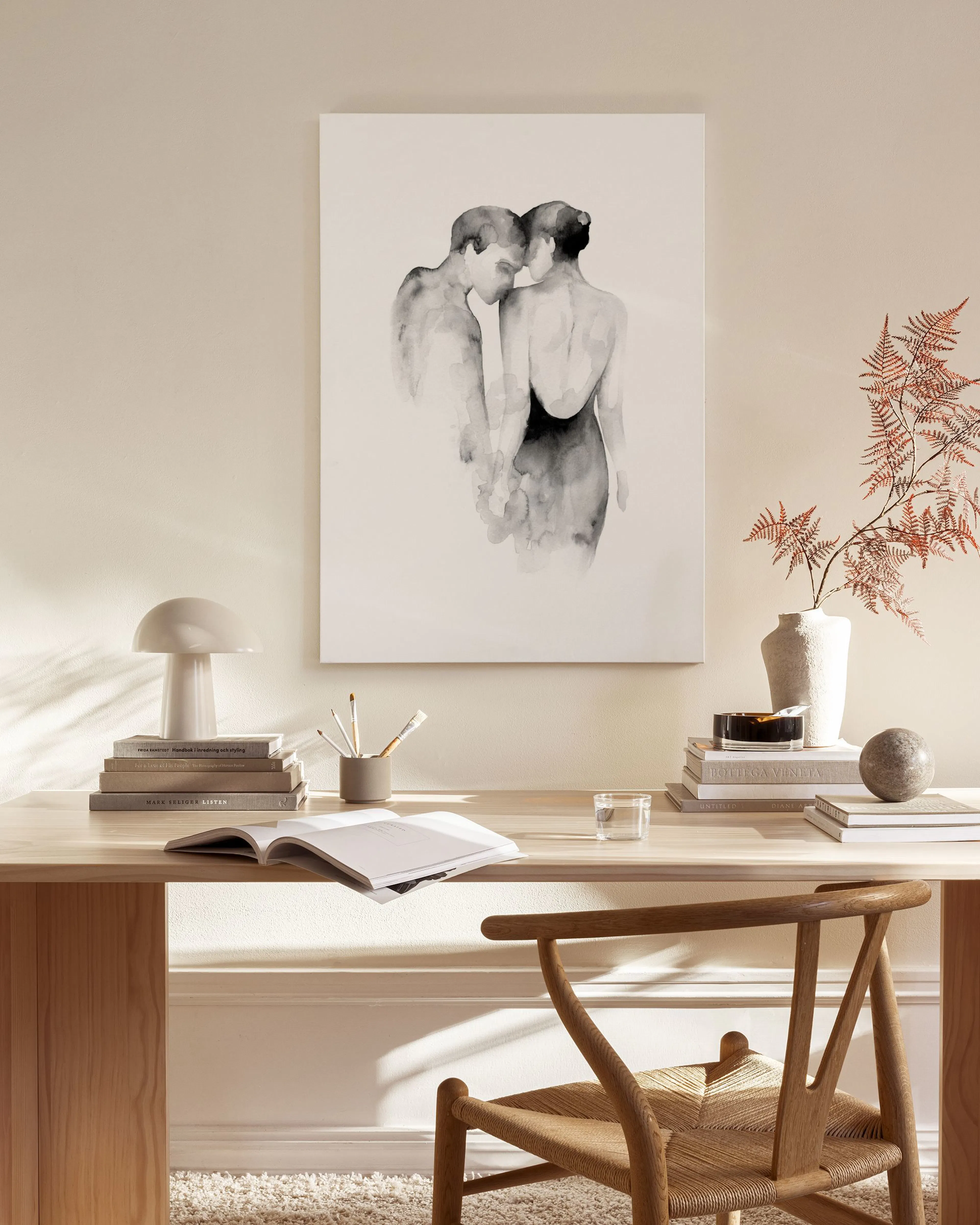 Lienzo de dos figuras femeninas en acuarela negra y gris, colgado sobre un mueble de madera en una sala de estar minimalista.