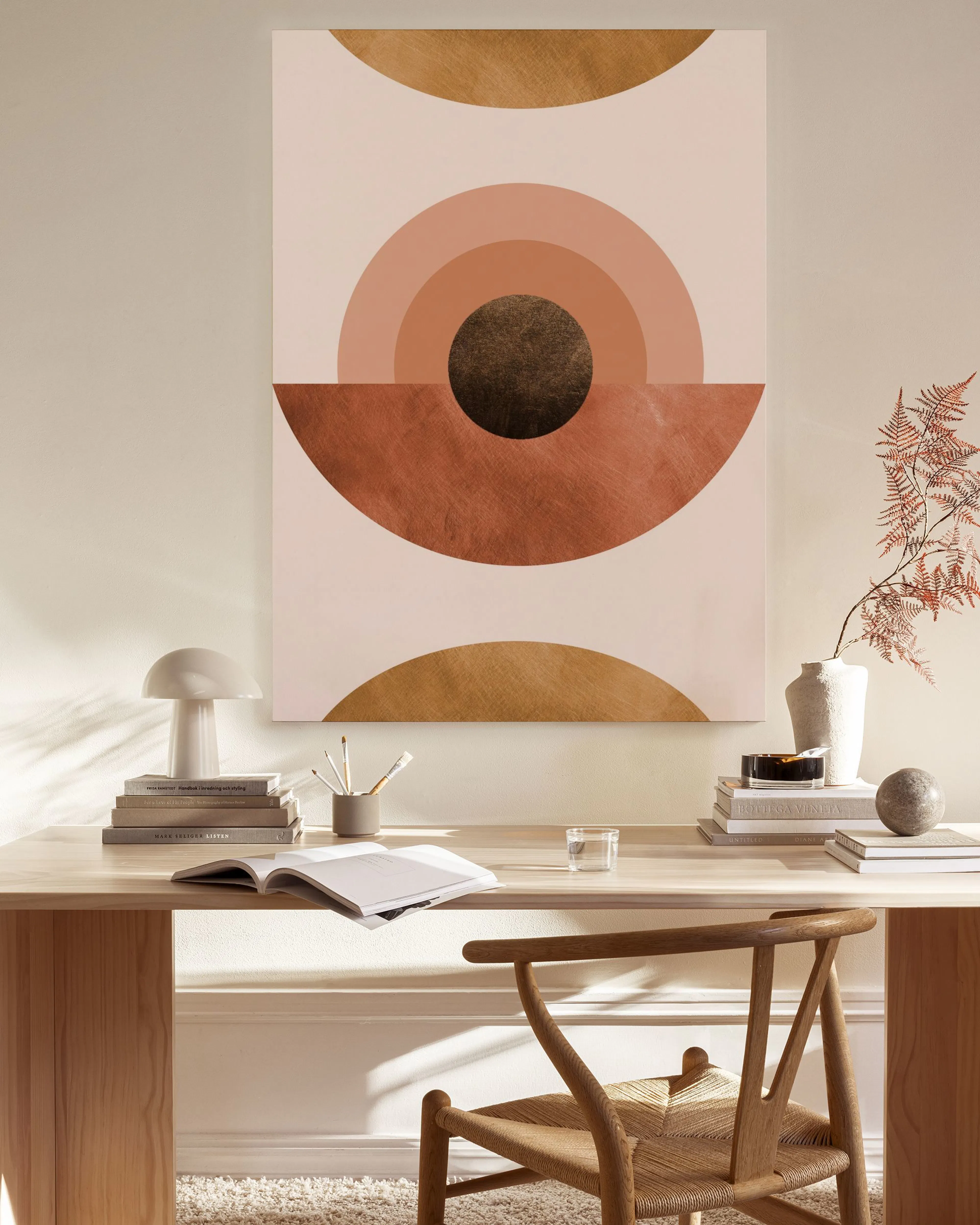 Lærred med geometrisk kunst i gyldne, brune og rosa nuancer, hængende i en stue over en træbænk.