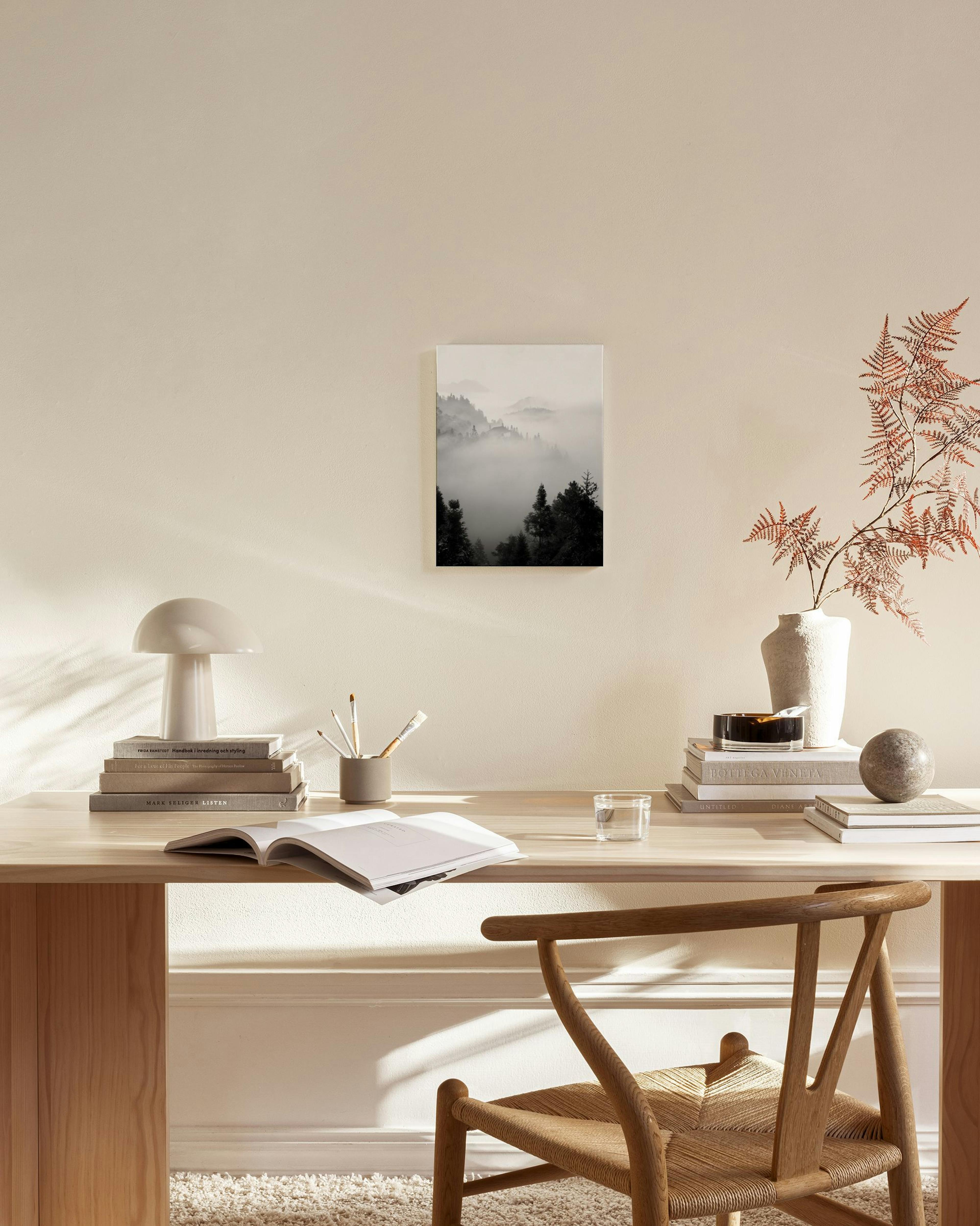 Canvas met een zwart-wit landschap van mistige bergen en donkere dennenbomen, hangend in een moderne woonkamer.
