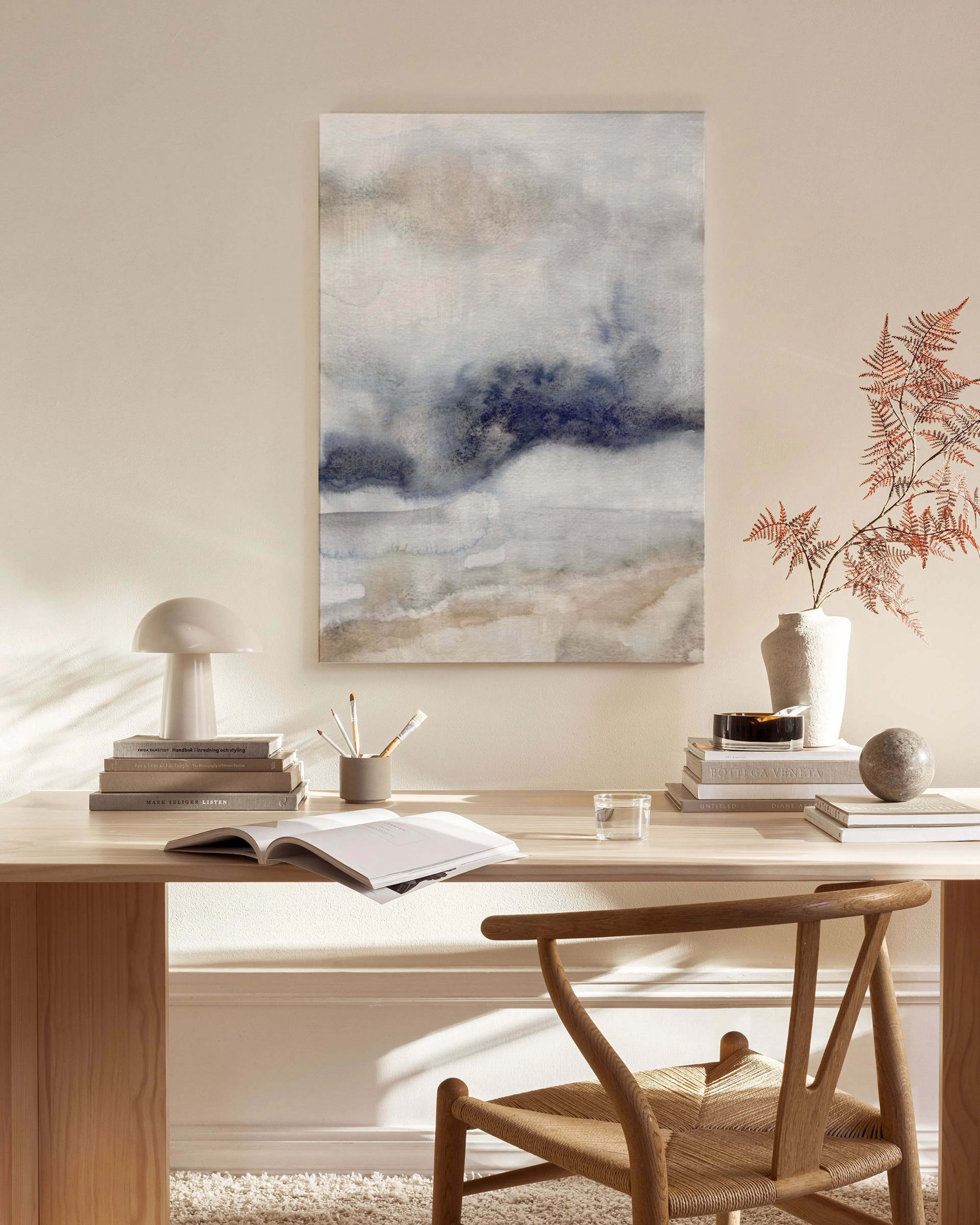 Lærred med abstrakt kunst i blå, beige og hvide nuancer, hængende over et lavt træmøbel i en stue.