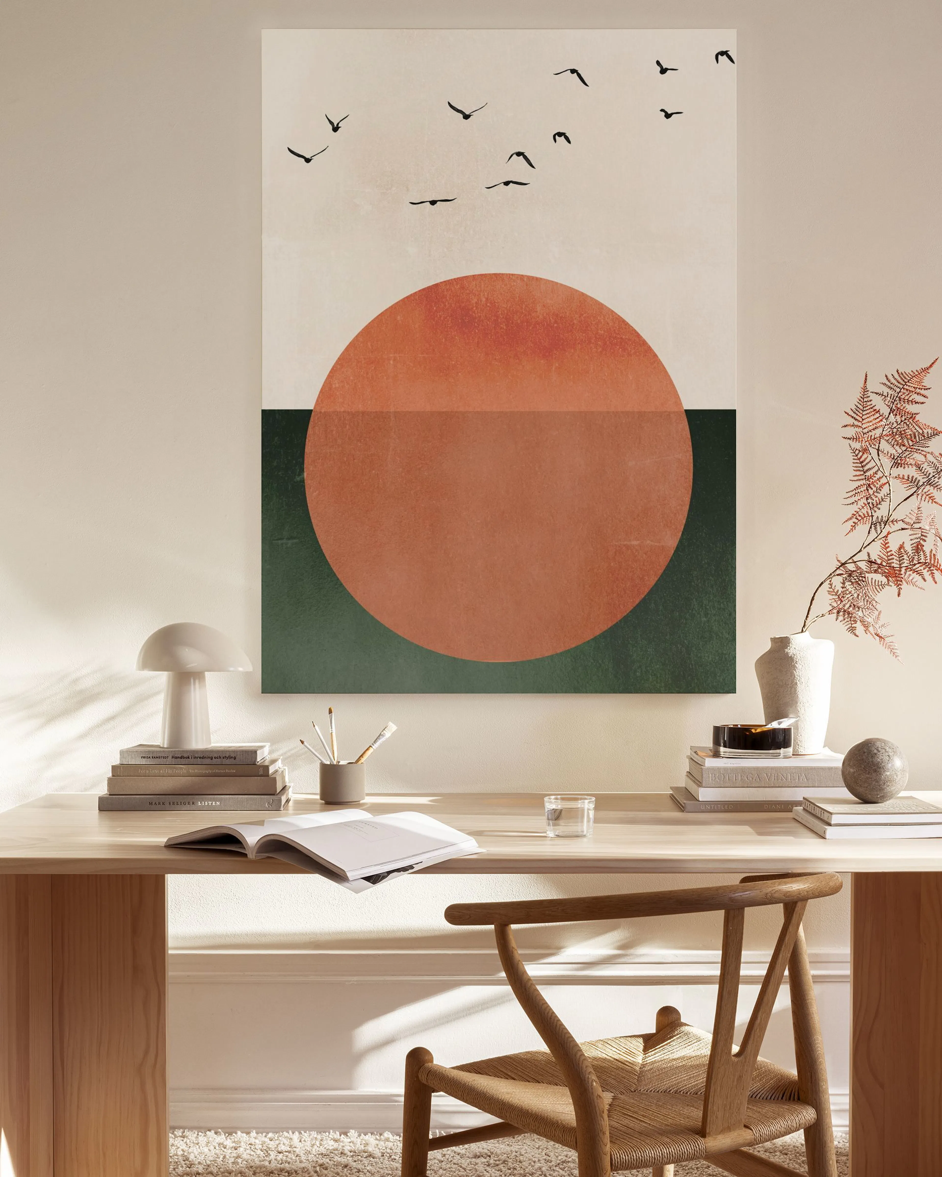 Canvas met roodbruine cirkel op donkergroen vlak, en zwarte vogels op een lichte achtergrond, hangend in een moderne woonkamer.