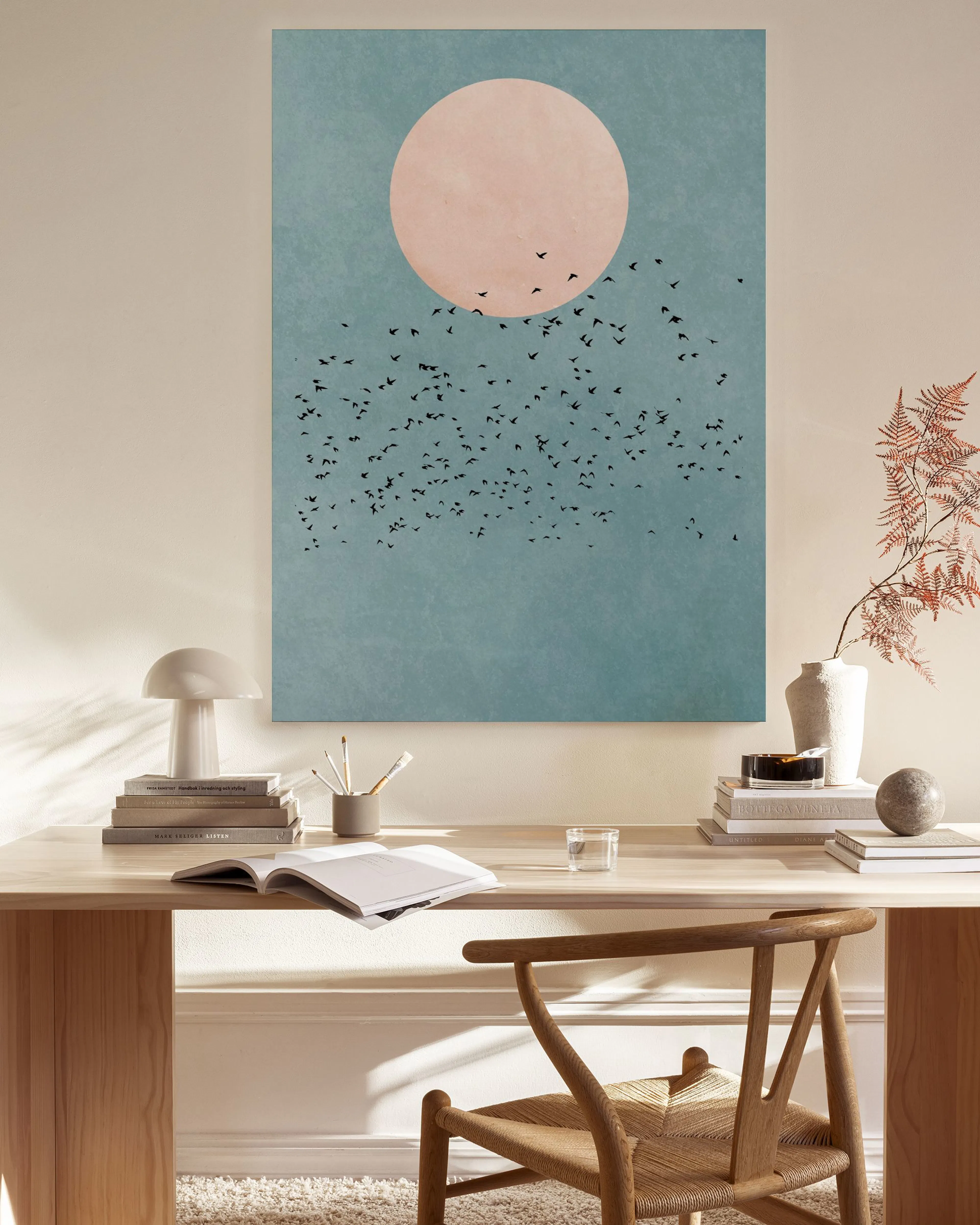 A canvas print of a pink moon and flock of birds against a blue sky, hanging in a minimalist living room.
