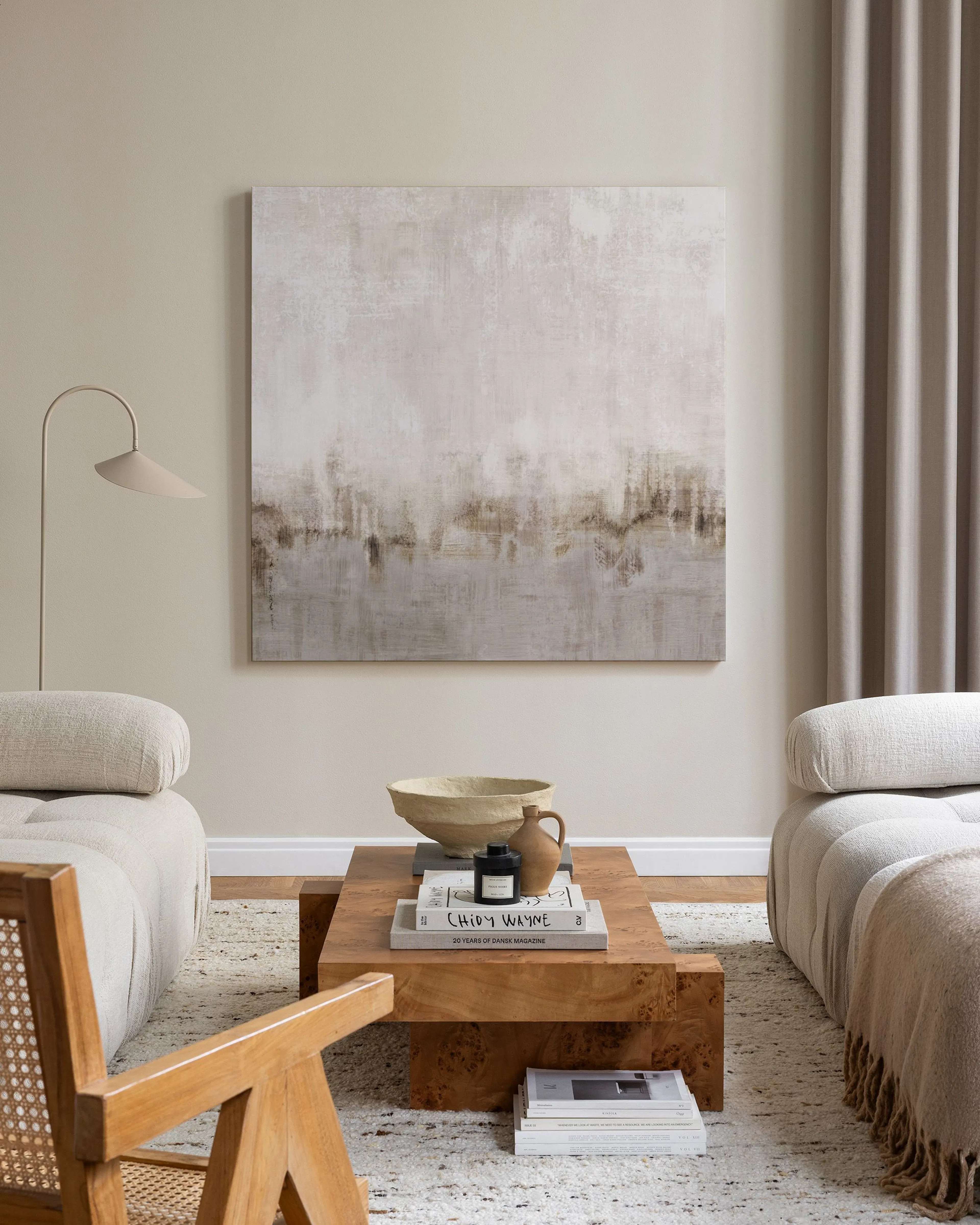 Canvastavla med abstrakt landskap i beige och brunt hängandes ovanför en bänk med böcker i ett modernt vardagsrum.