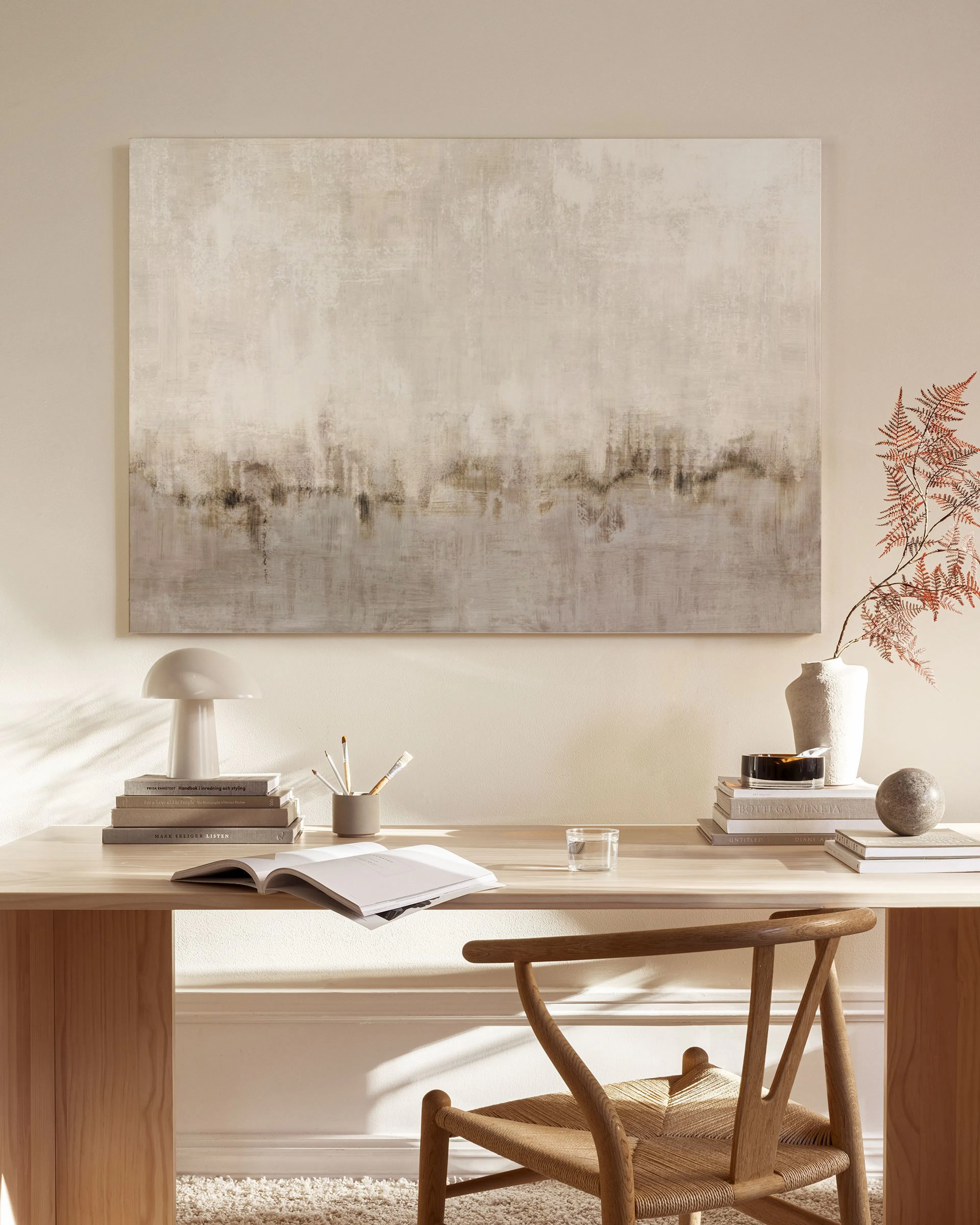 Abstract canvas print with a textured beige and brown landscape, hanging above a wooden console in a minimalist living room.