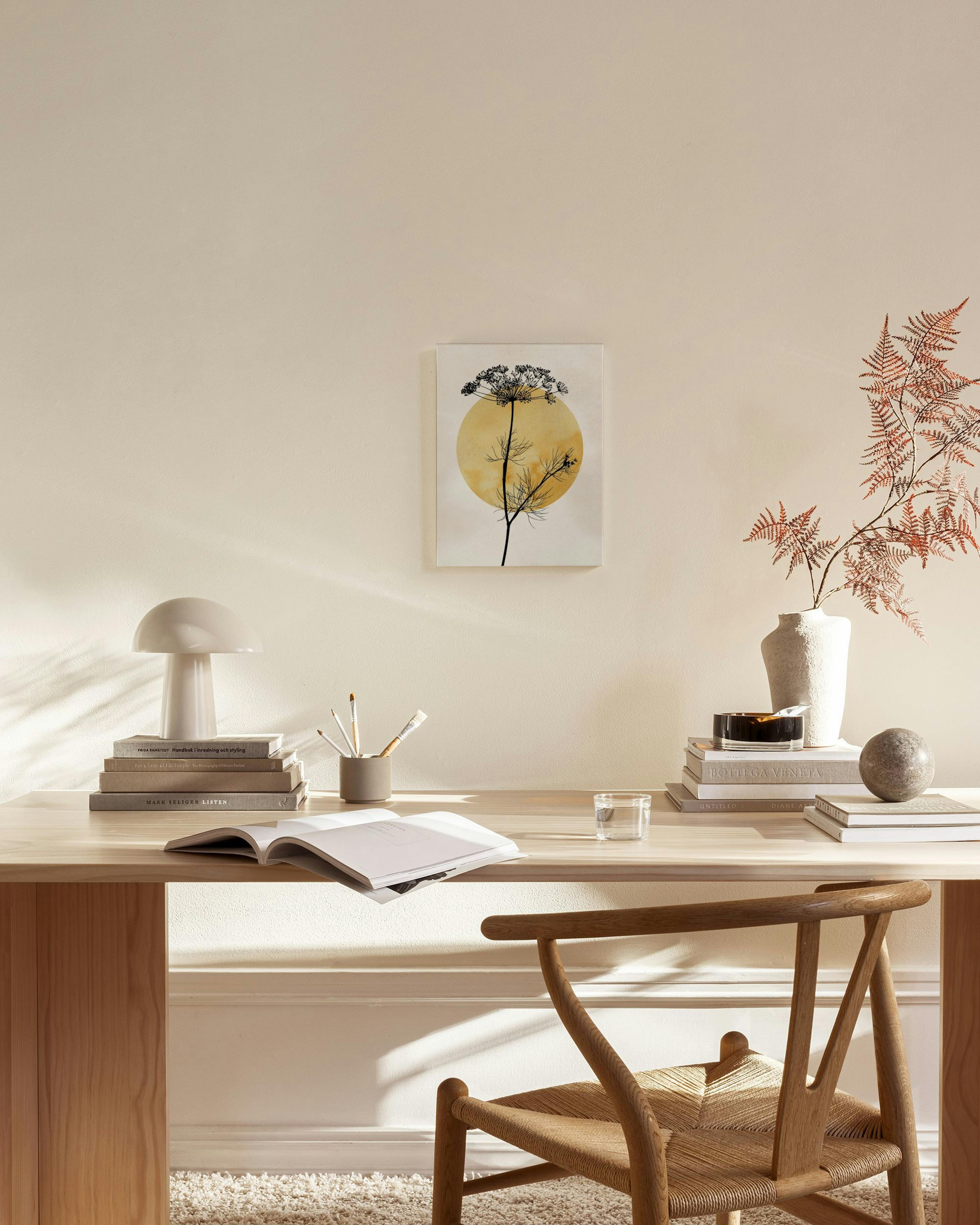 A canvas print of a black botanical silhouette with a yellow circle background, hanging in a minimalist living room.