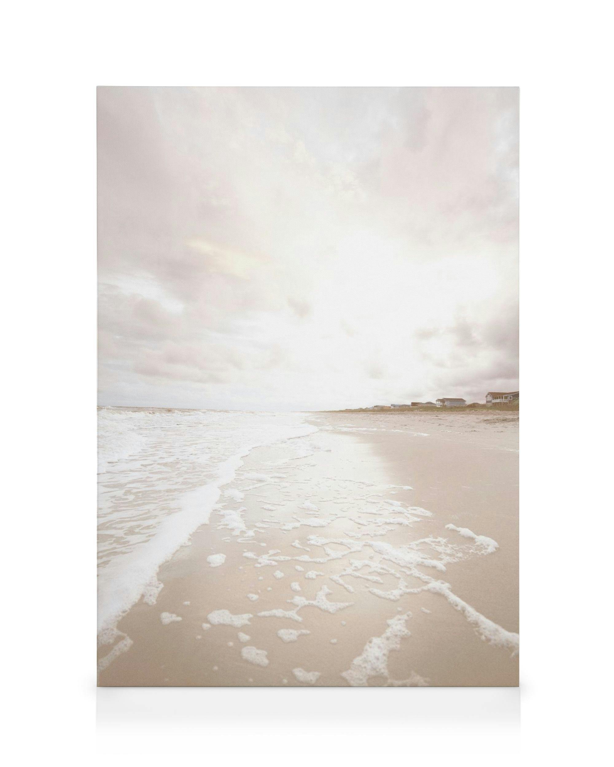 Fotografia béžovej pláže s morskou penou, domami a zamračenou oblohou