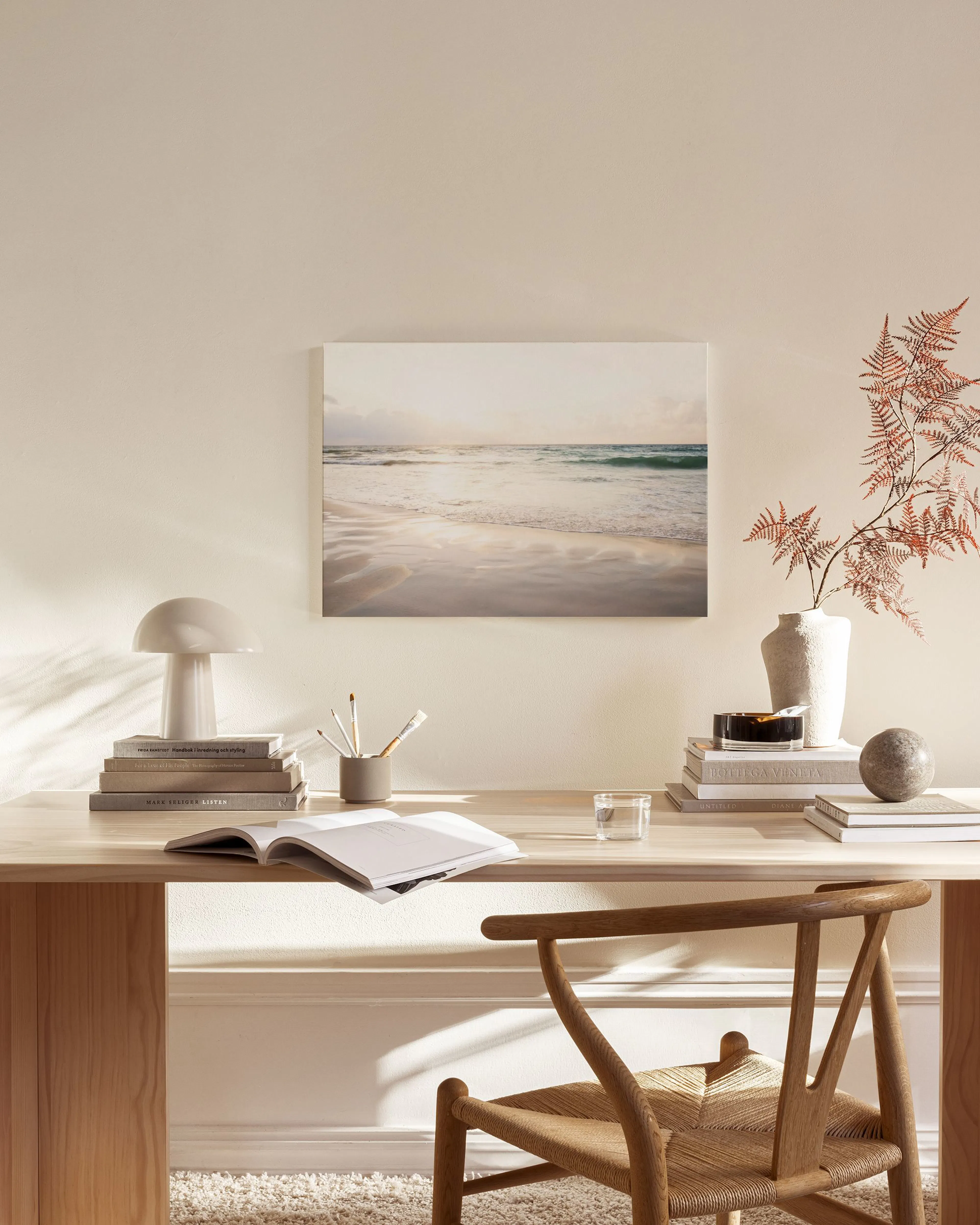Canvastavla med strandmotiv hängandes ovanför en bänk med böcker i ett ljust vardagsrum.