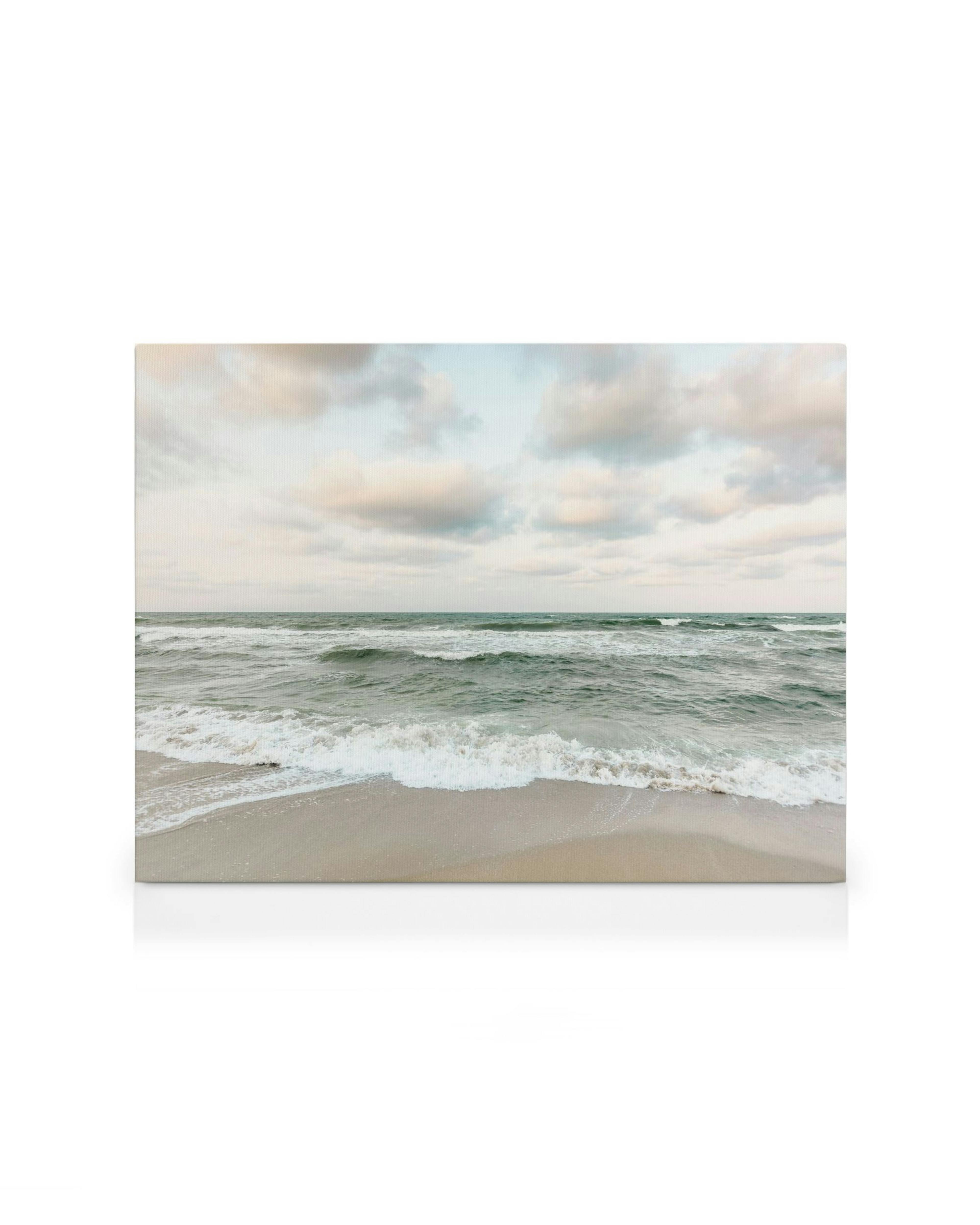 Fotografie einer Küstenlinie mit blaugrünem Meer, Wellen, Sandstrand und bewölktem Himmel