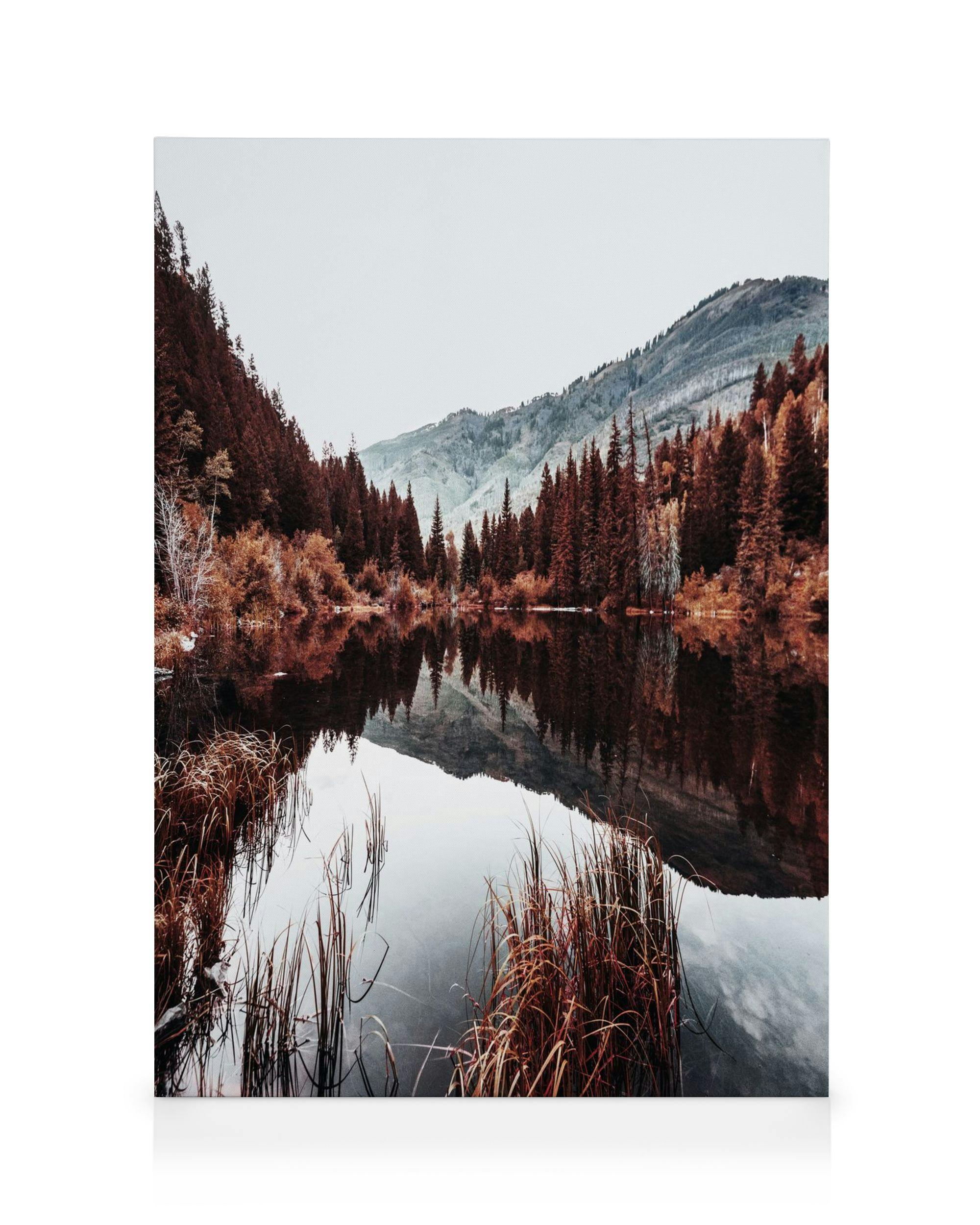 Toile paysage lac automnal reflétant des arbres aux feuilles rousses et montagnes sous un ciel nuageux, couleurs tamisées.