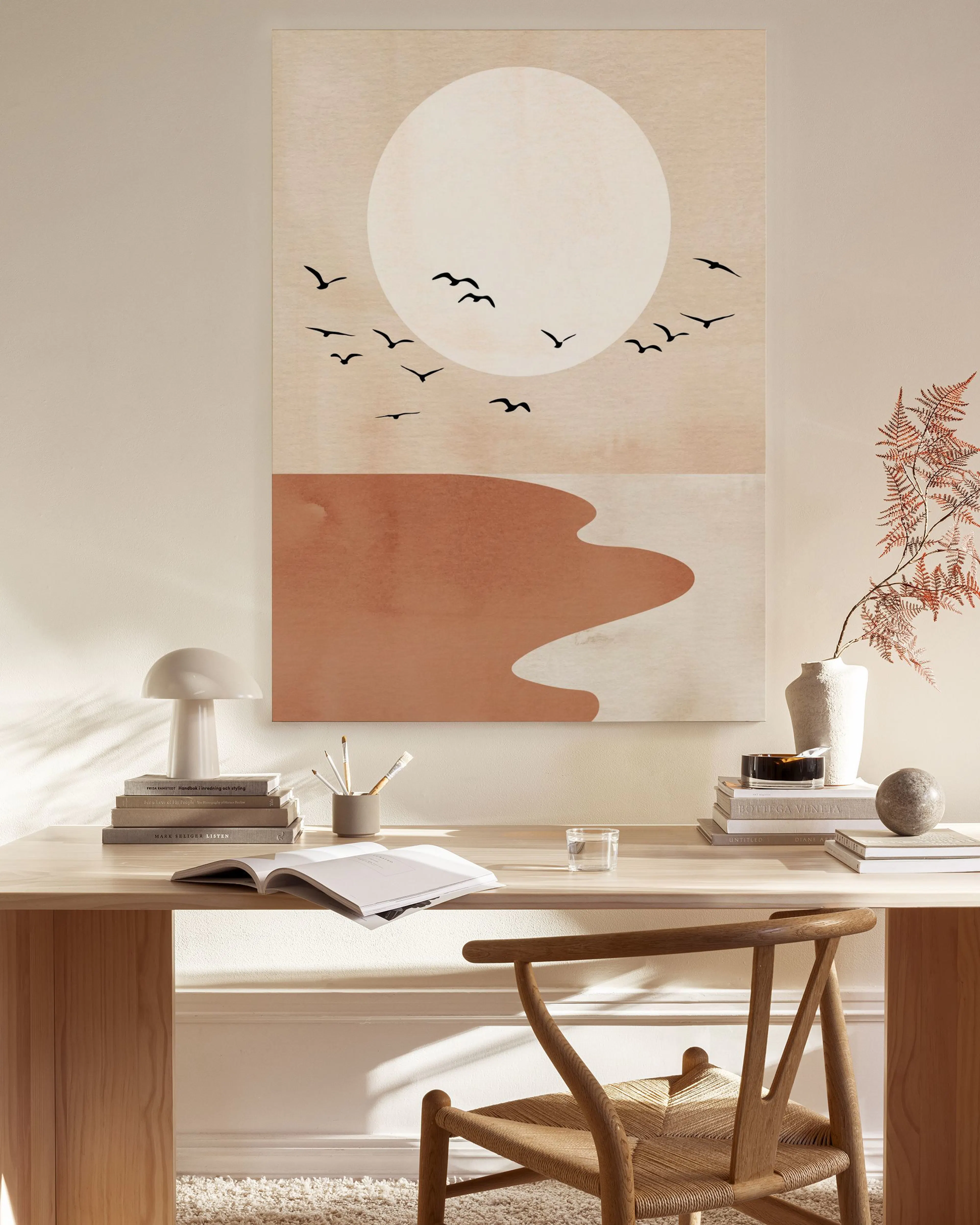 A canvas print of a minimalist desert landscape with a large white sun and flock of birds, hanging in a neutral living room.