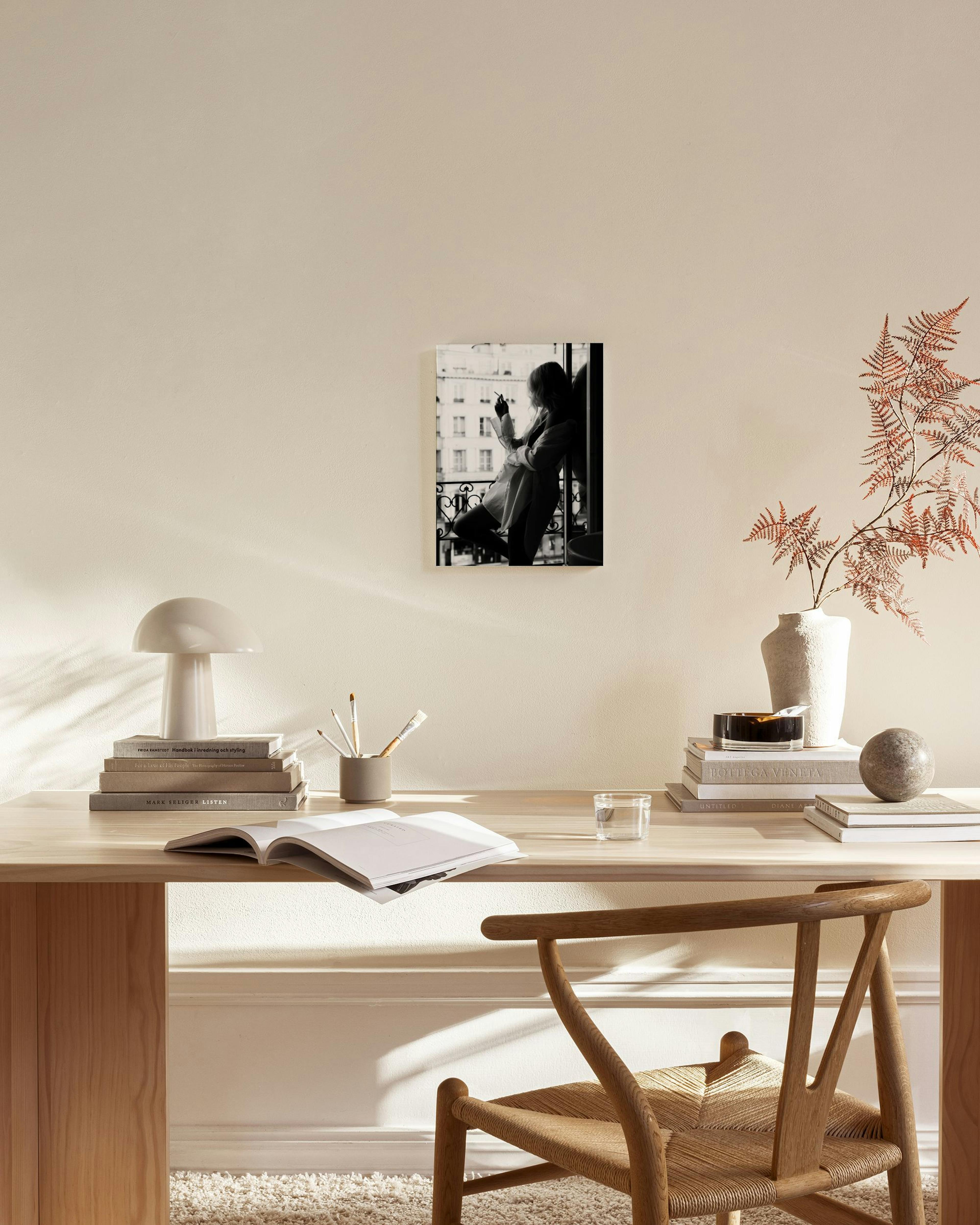 Zwart-wit canvas van een vrouw die op een balkon rookt, hangend in een moderne woonkamer boven een dressoir.