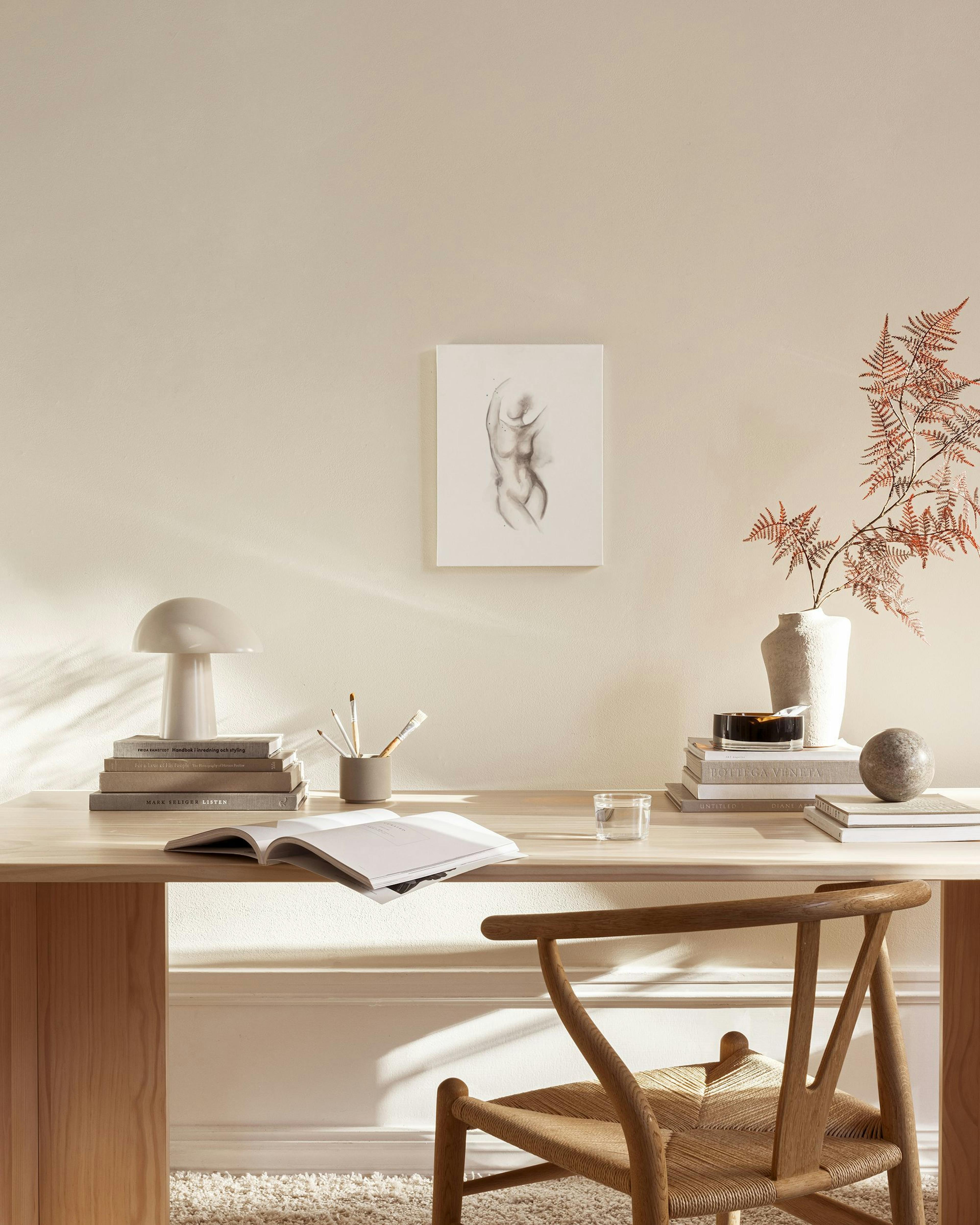 Tela decorativa com desenho a aguarela de um torso feminino em tons neutros, pendurada numa sala de estar com mobiliário de made