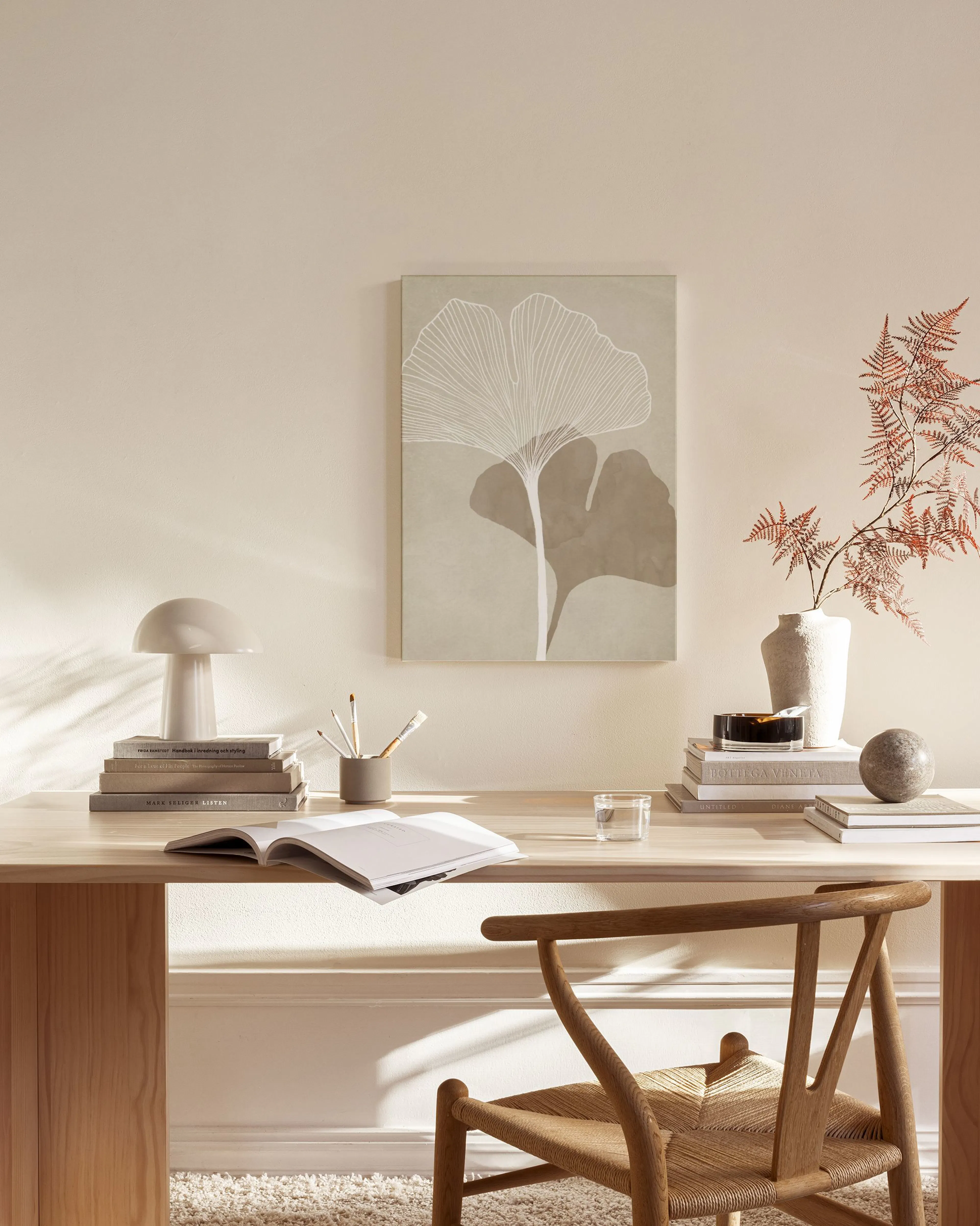 Stampa su tela con foglie di ginkgo stilizzate, bianche e beige, appesa in un soggiorno moderno.