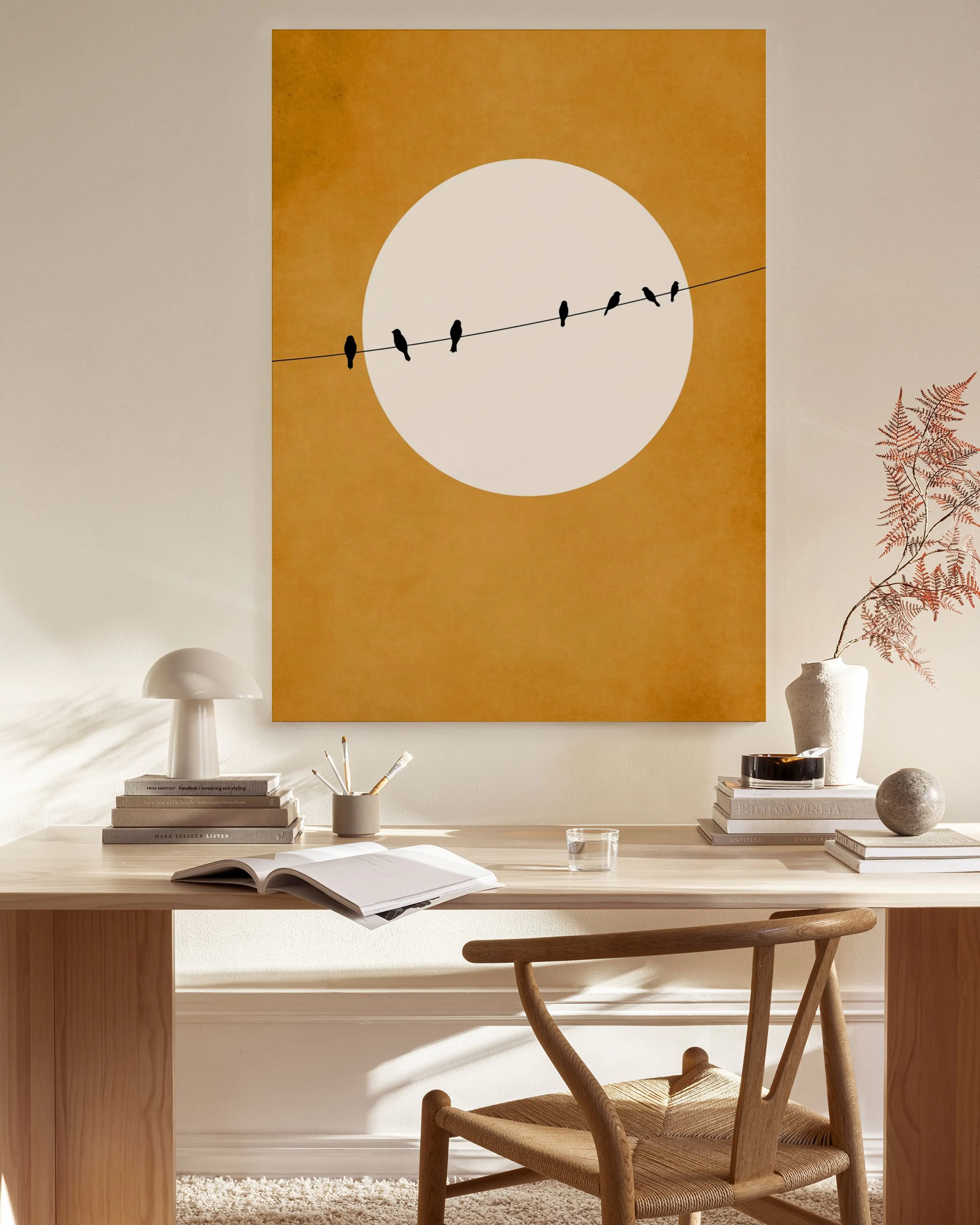 Toile minimaliste avec oiseaux sur fil devant un soleil blanc sur fond ocre, affichée dans un salon moderne et lumineux.