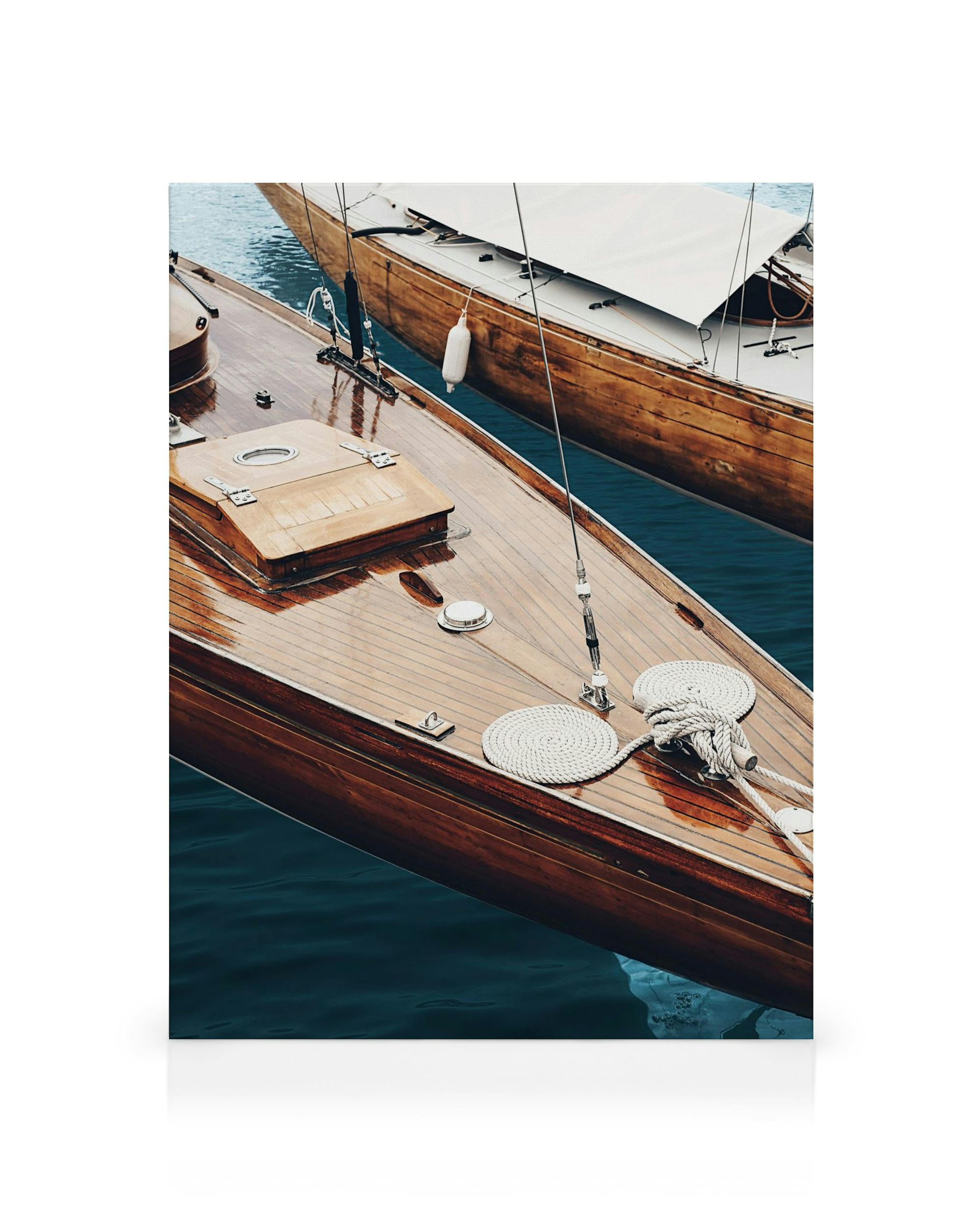 Toile présentant le pont en bois dun bateau classique, avec des cordes enroulées et une voile, sur une eau bleu foncé.