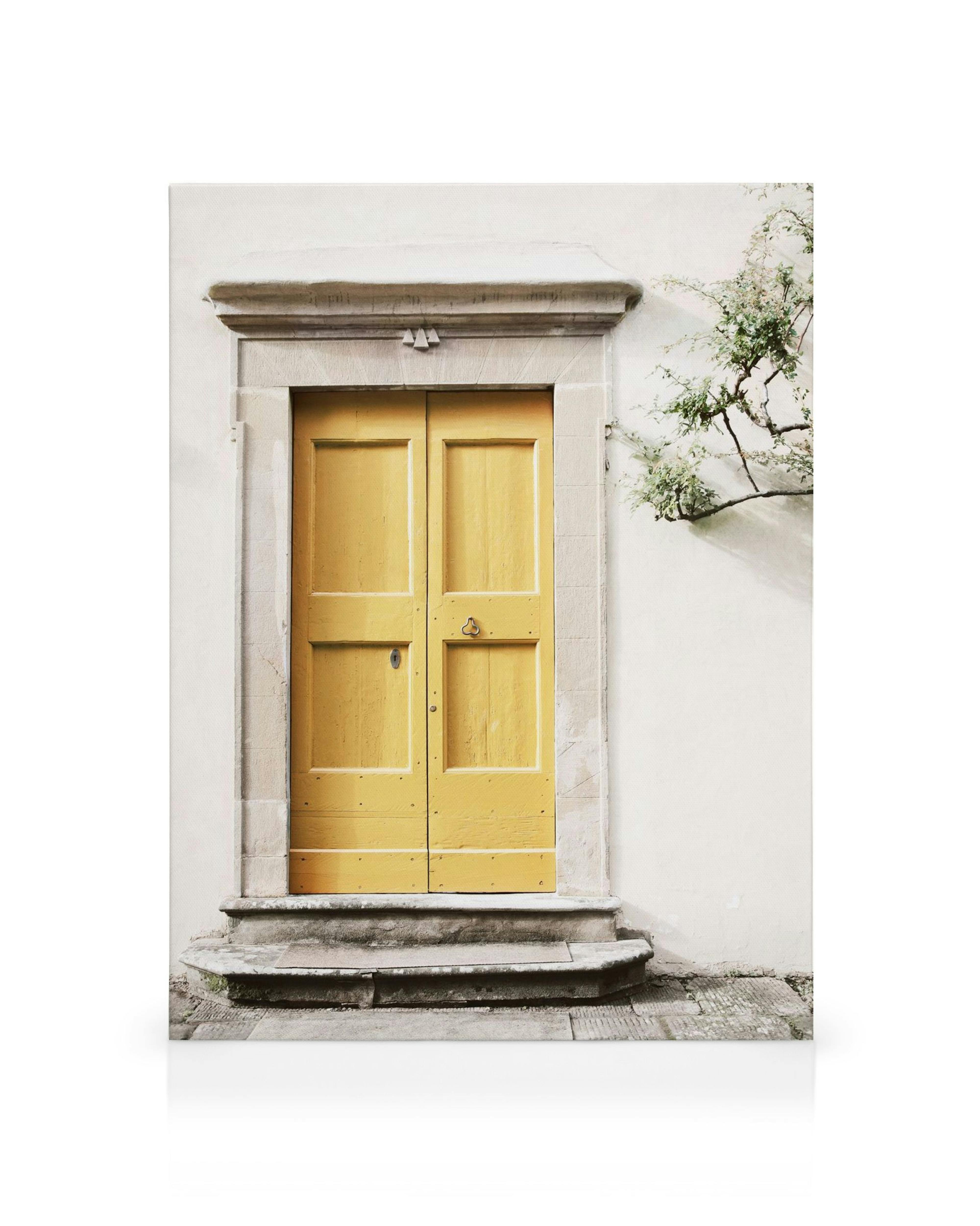 Leinwandbild einer leuchtend gelben Holztür in einer weißen Steinmauer mit Stufen und einer Pflanze