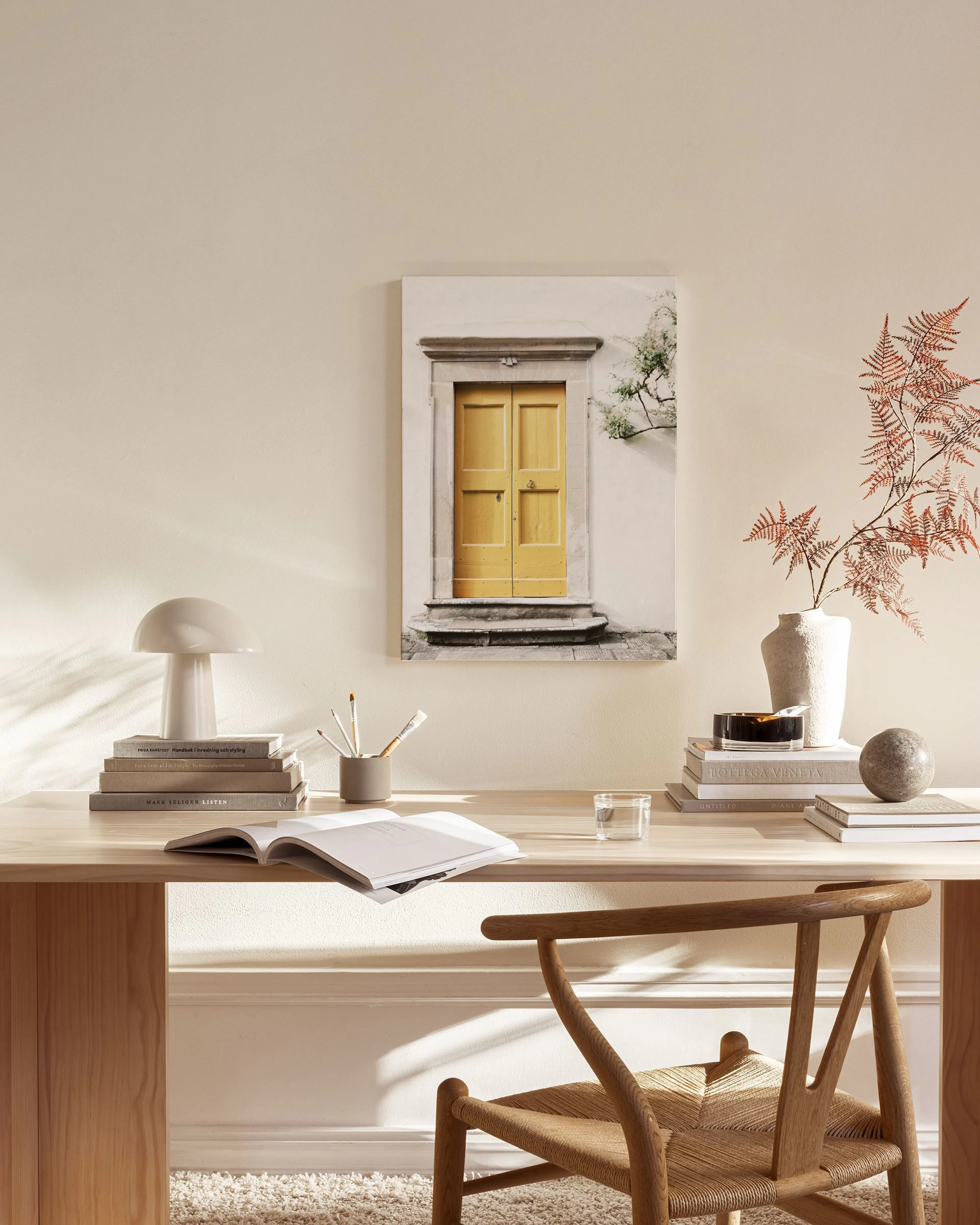 A canvas print of a vibrant yellow door with stone steps and green foliage, hanging in a minimalist living room.