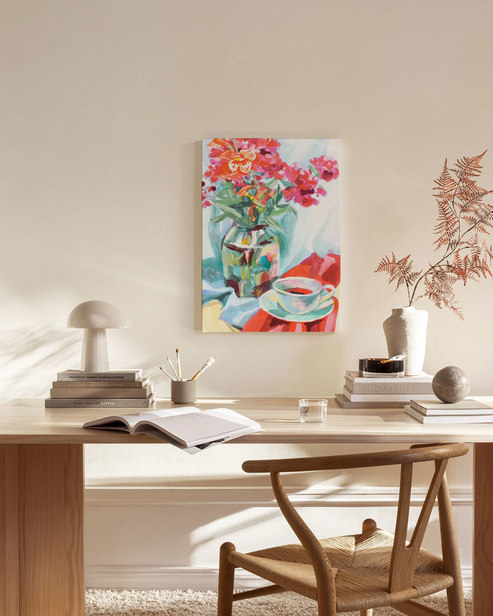 Toile de nature morte avec des fleurs rouges dans un vase et une tasse, suspendue dans un salon moderne.