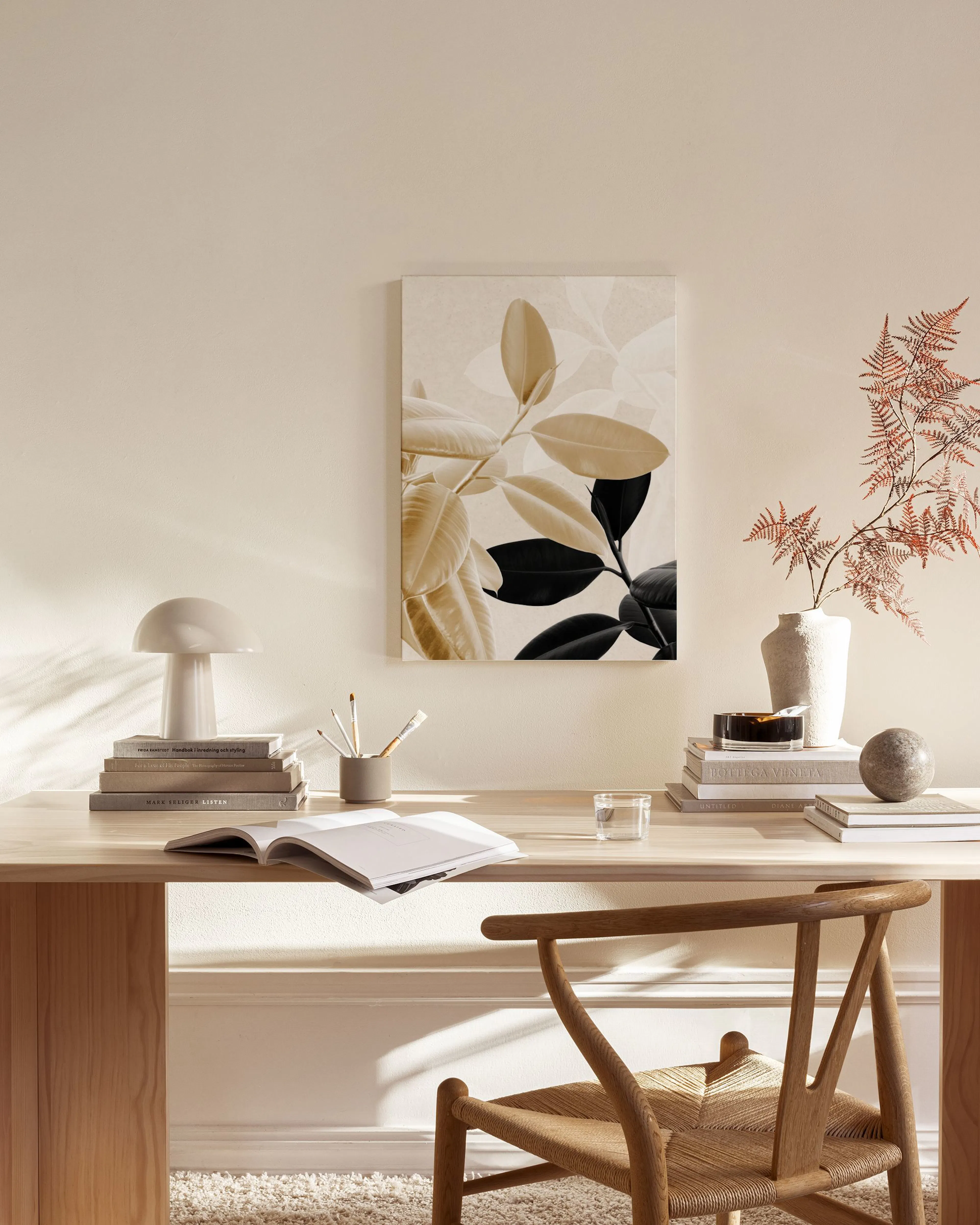 Lærred med et botanisk motiv med beige og sorte blade, hængende over et sidebord i en stue.