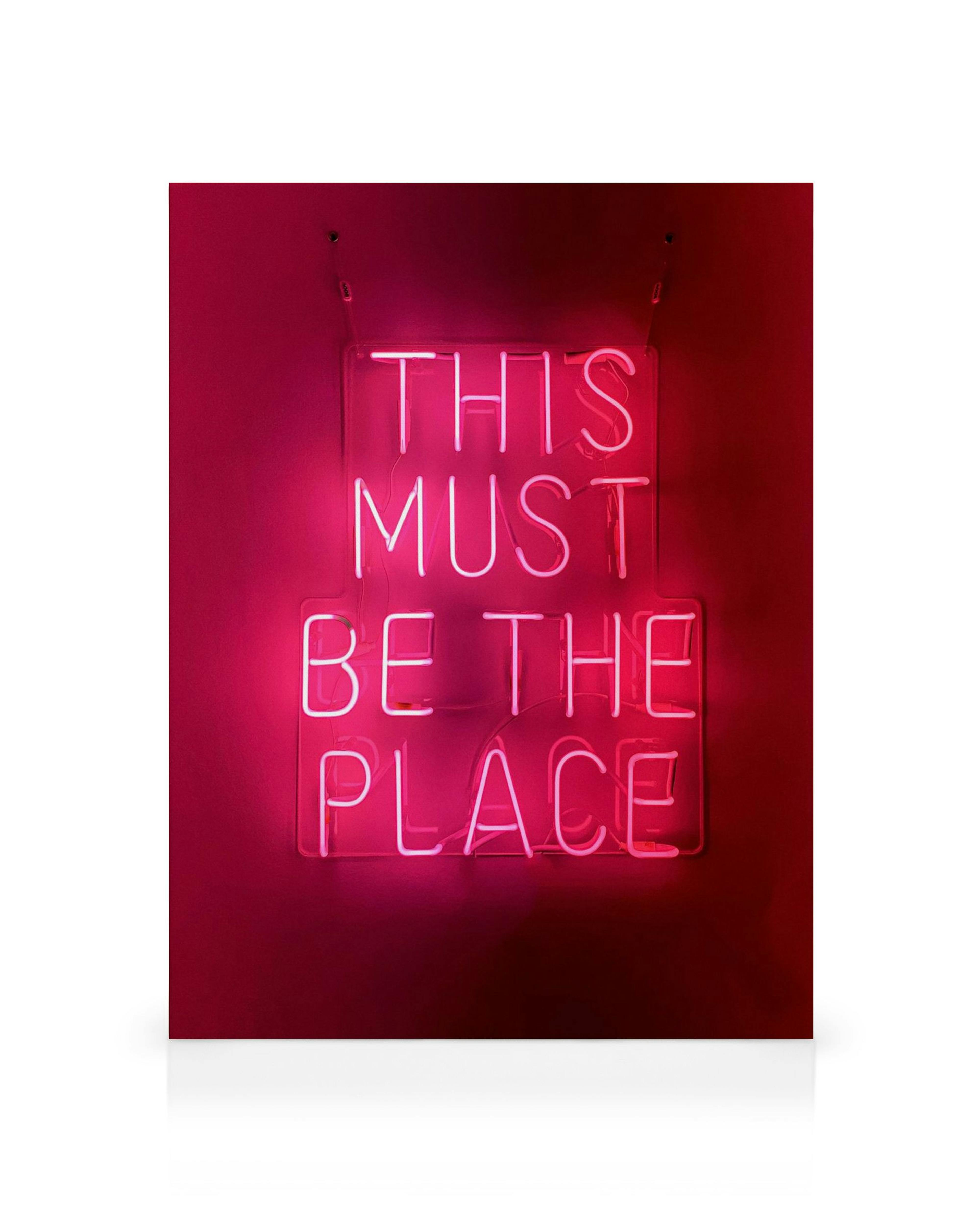 Neon sign canvas print with This Must Be The Place in bright pink against a dark pink wall.