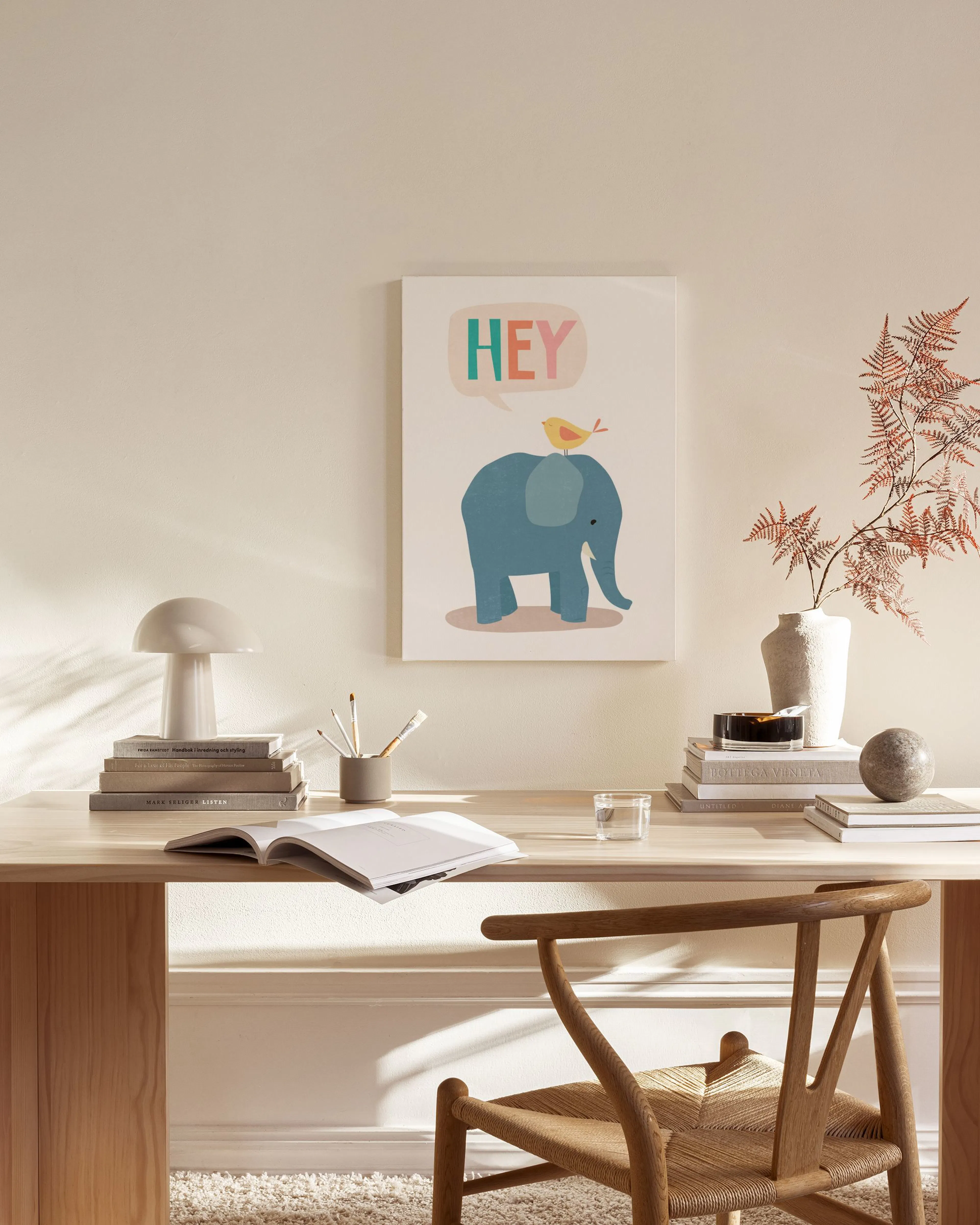 A canvas print of a blue elephant with a yellow bird and HEY text, displayed in a living room above a wooden console.