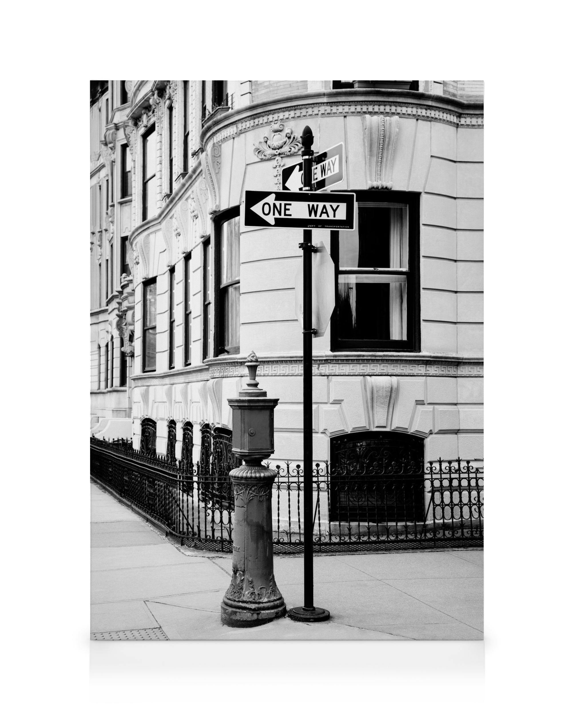 Black and white cityscape canvas print featuring a street corner with a one-way sign, fire hydrant, and ornate building.