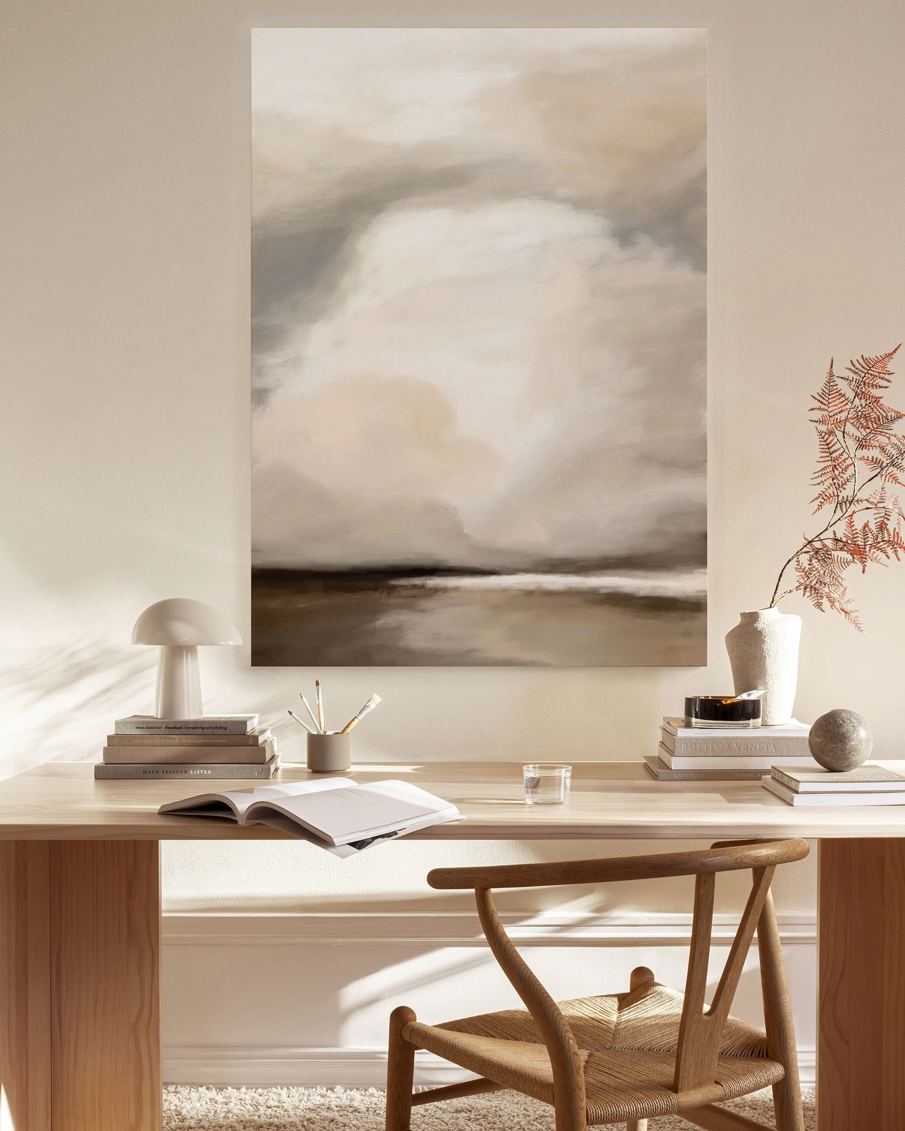 Leinwandbild mit Landschaft in Beige- und Brauntönen, über einem Holzmöbel in einem hellen Wohnzimmer.